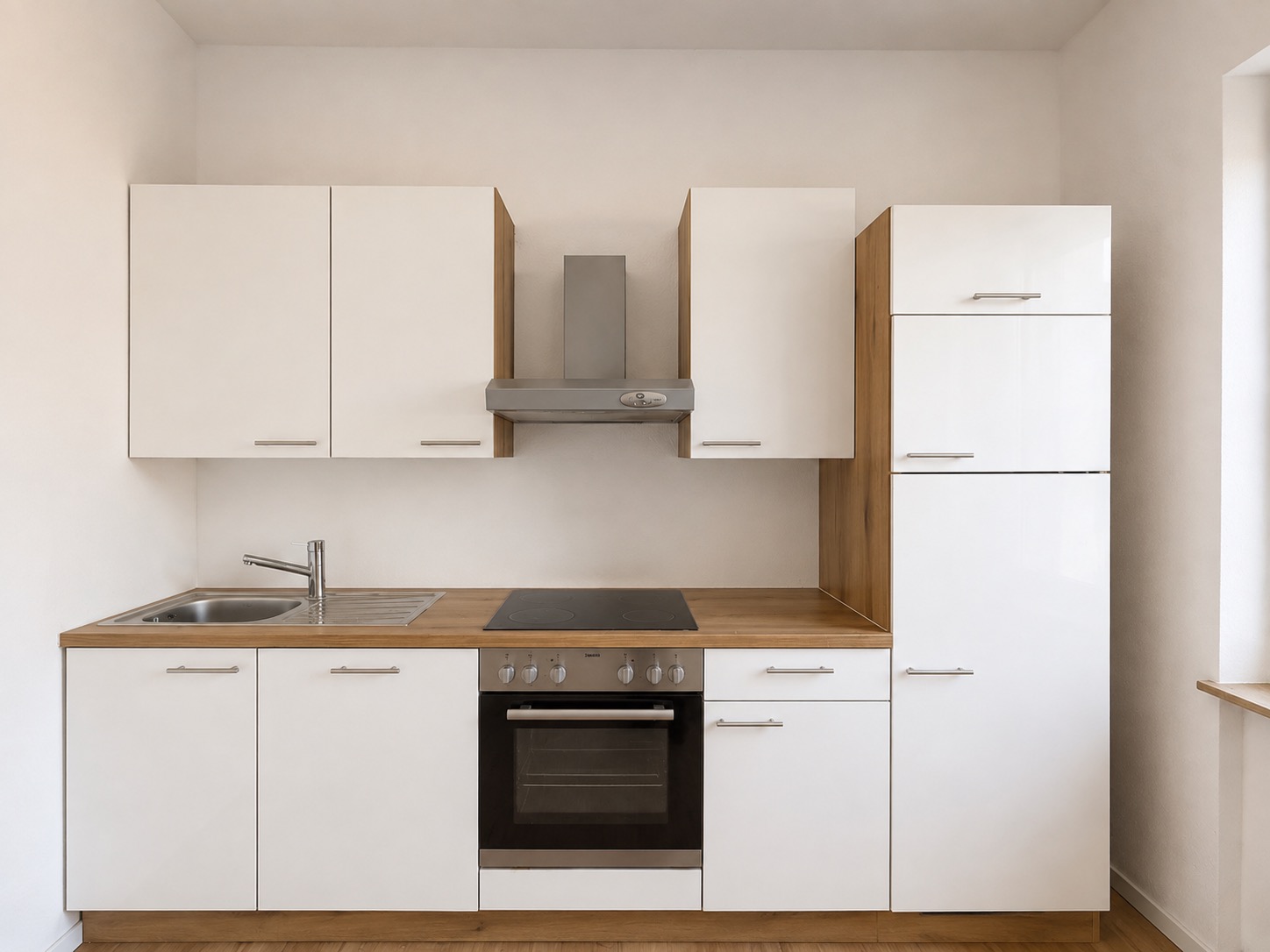 Moderne, weiße Einbauküche mit Spüle, Herd, Backofen und Hängeschränken.