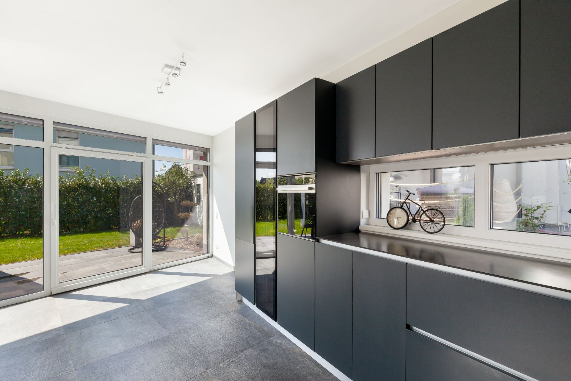 Moderne Küche mit schwarzen Schränken, großem Fenster und Blick auf Garten und Terrasse.