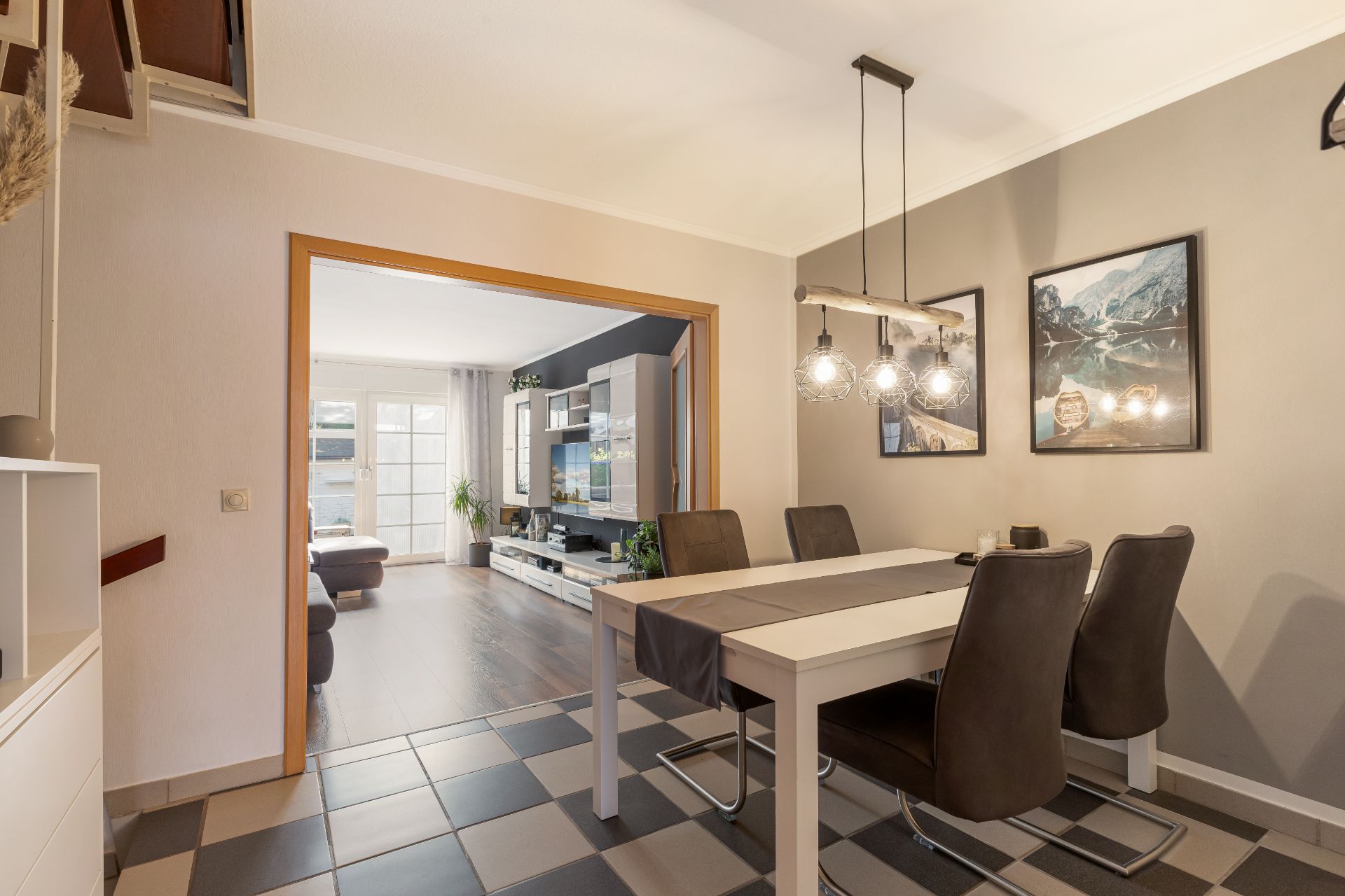 Esszimmer mit weißem Tisch, vier Stühlen und moderner Lampe, Blick ins Wohnzimmer mit TV und Sofa.