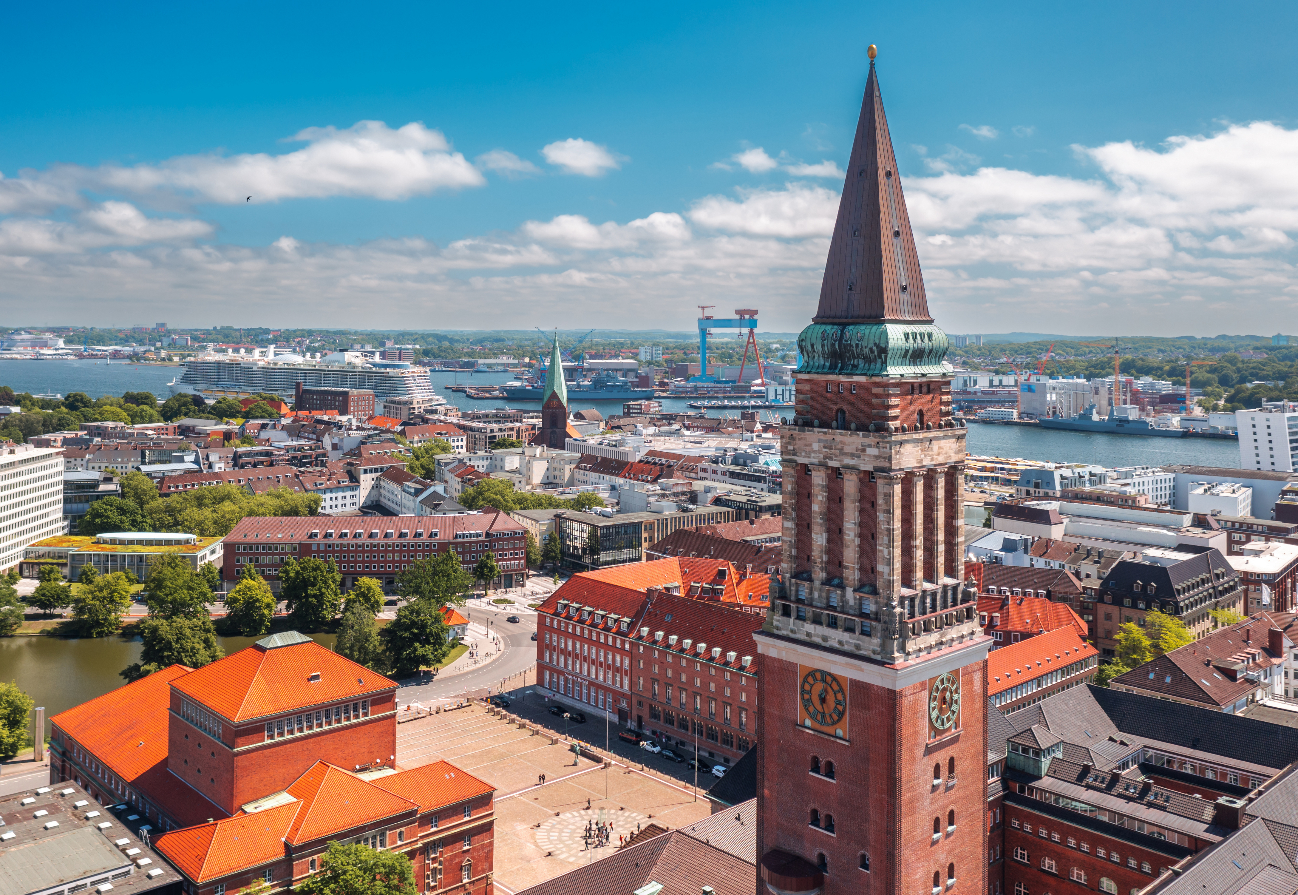 Blick auf einen großen Backsteinturm mit Uhr vor einer Stadt und einem Hafen im Hintergrund.