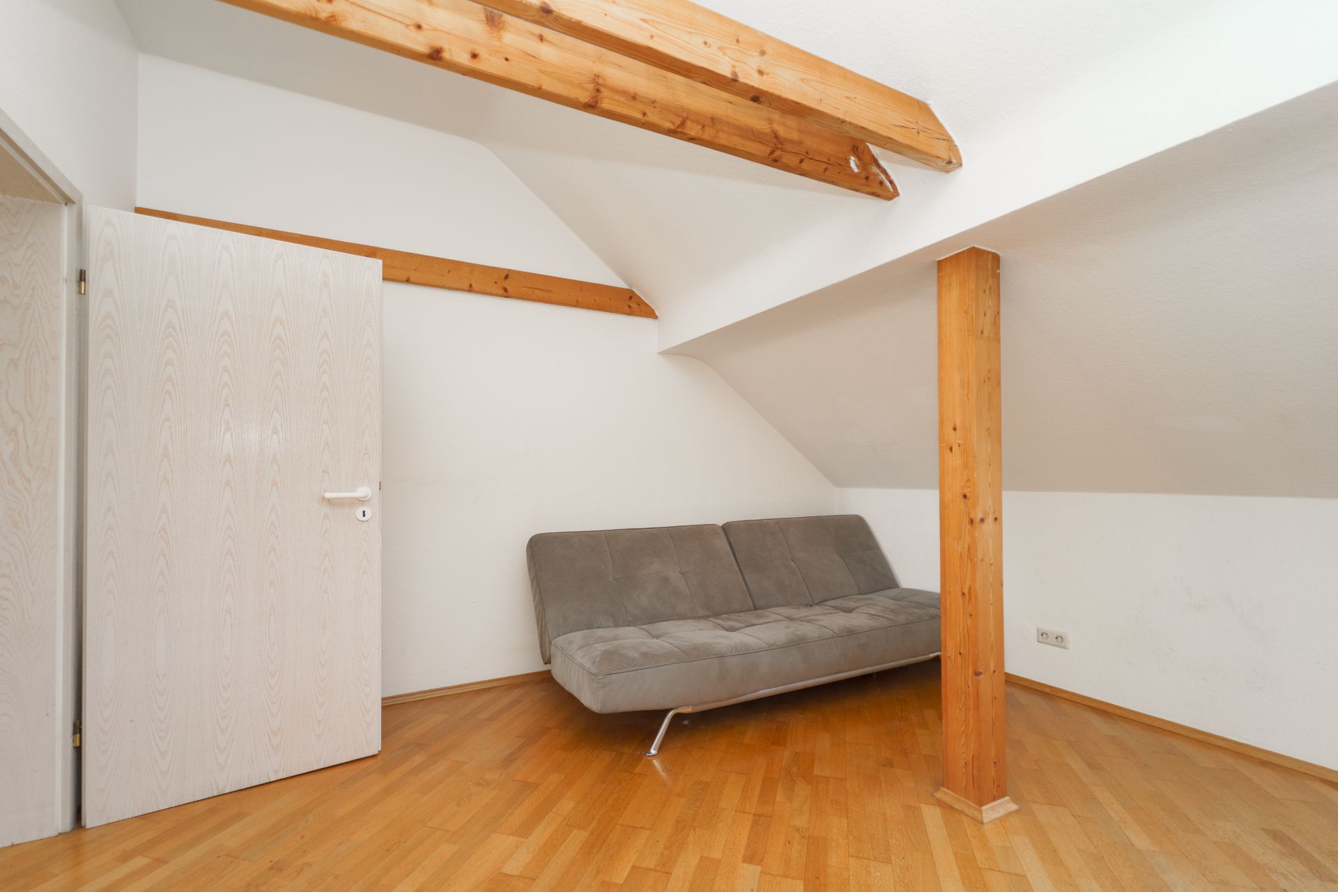 Dachzimmer mit Holzbalken, grauem Sofa, Holzboden und Stützpfeiler.