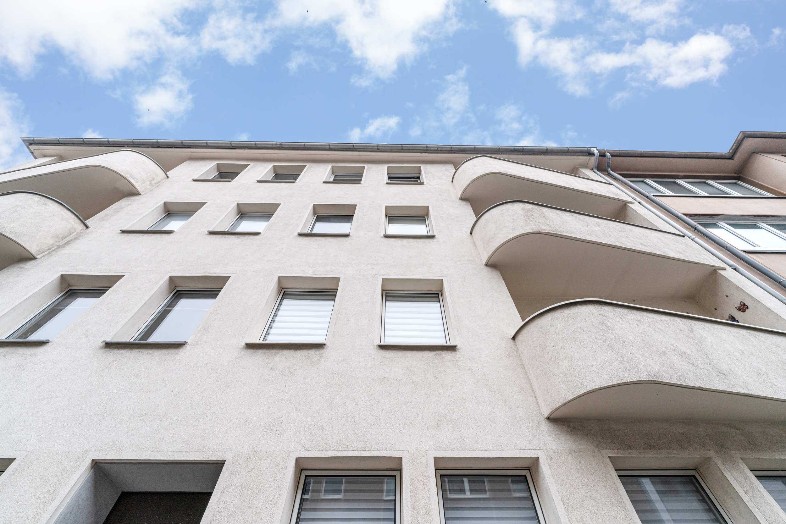 Fassade eines mehrstöckigen Wohnhauses mit mehreren Fenstern und Balkonen.