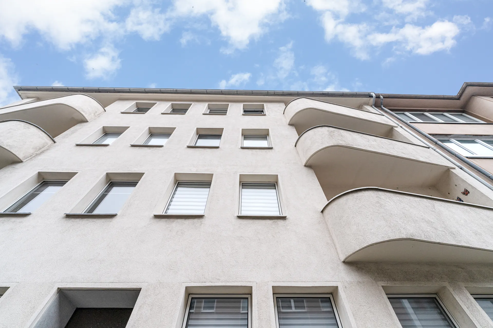 Fassade eines mehrstöckigen Wohnhauses mit mehreren Fenstern und Balkonen.