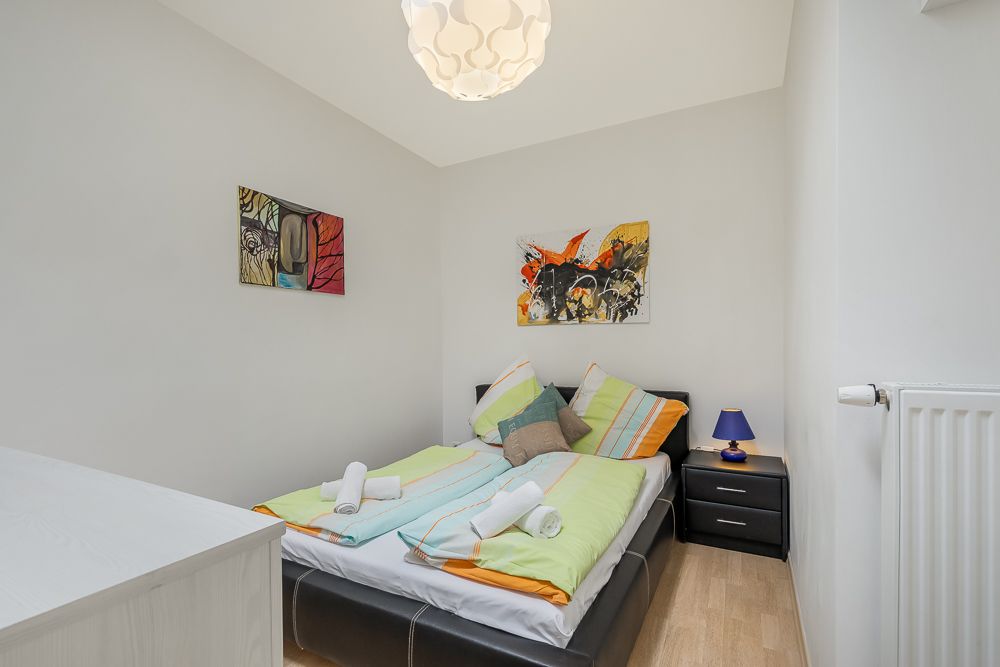 Kleines Schlafzimmer mit Doppelbett, bunter Bettwäsche, Nachttisch und Wandbildern.