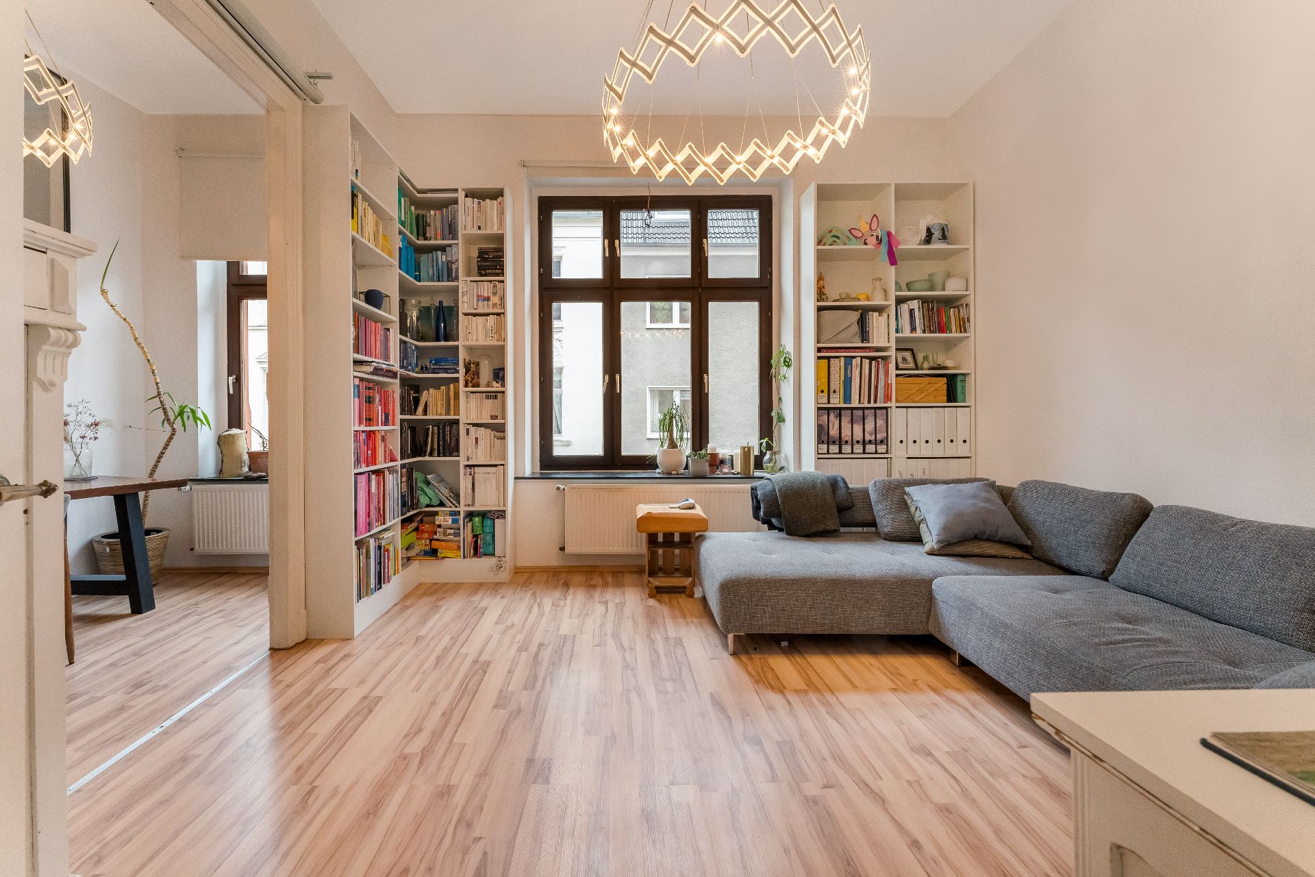 Helles Wohnzimmer mit grauem Sofa, Bücherregalen, Holzfußboden und großem Fenster.
