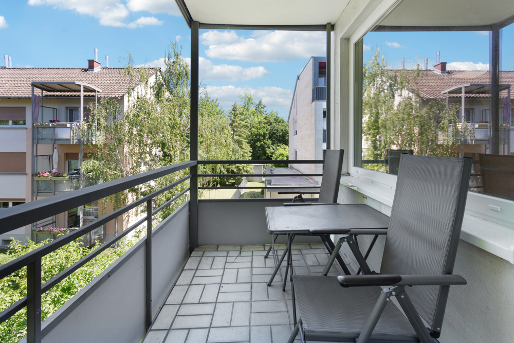 Balkon mit zwei Stühlen und einem Tisch, Blick auf andere Wohngebäude und Bäume.