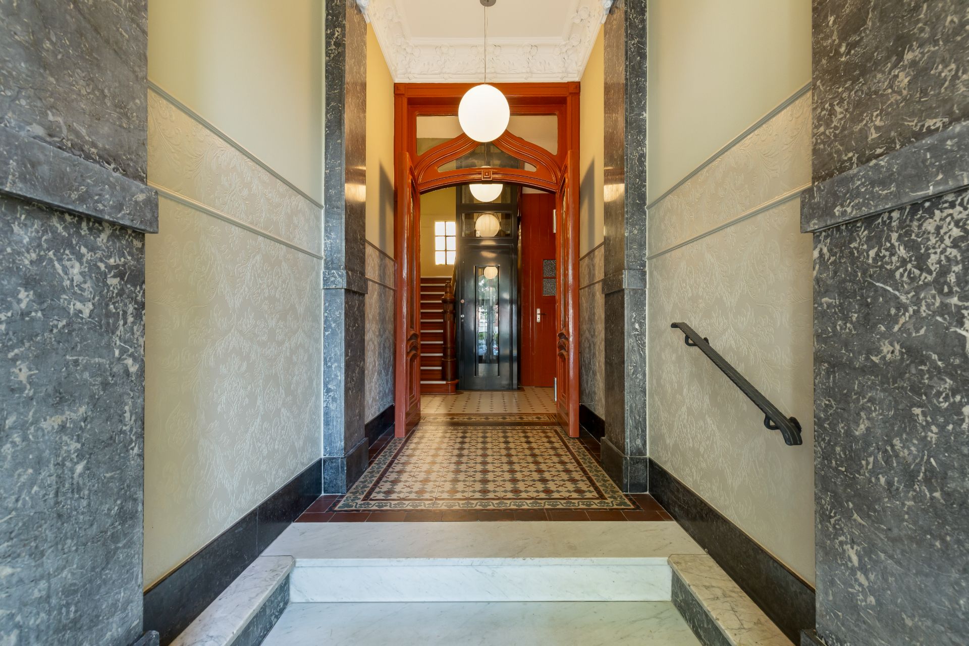Hausflur mit Marmorstufen, gemustertem Boden und Treppe im Hintergrund.