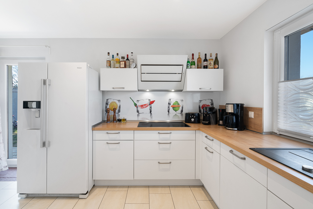 Moderne weiße Küche mit großem Kühlschrank, Holzarbeitsplatte und verschiedenen Küchenmaschinen.