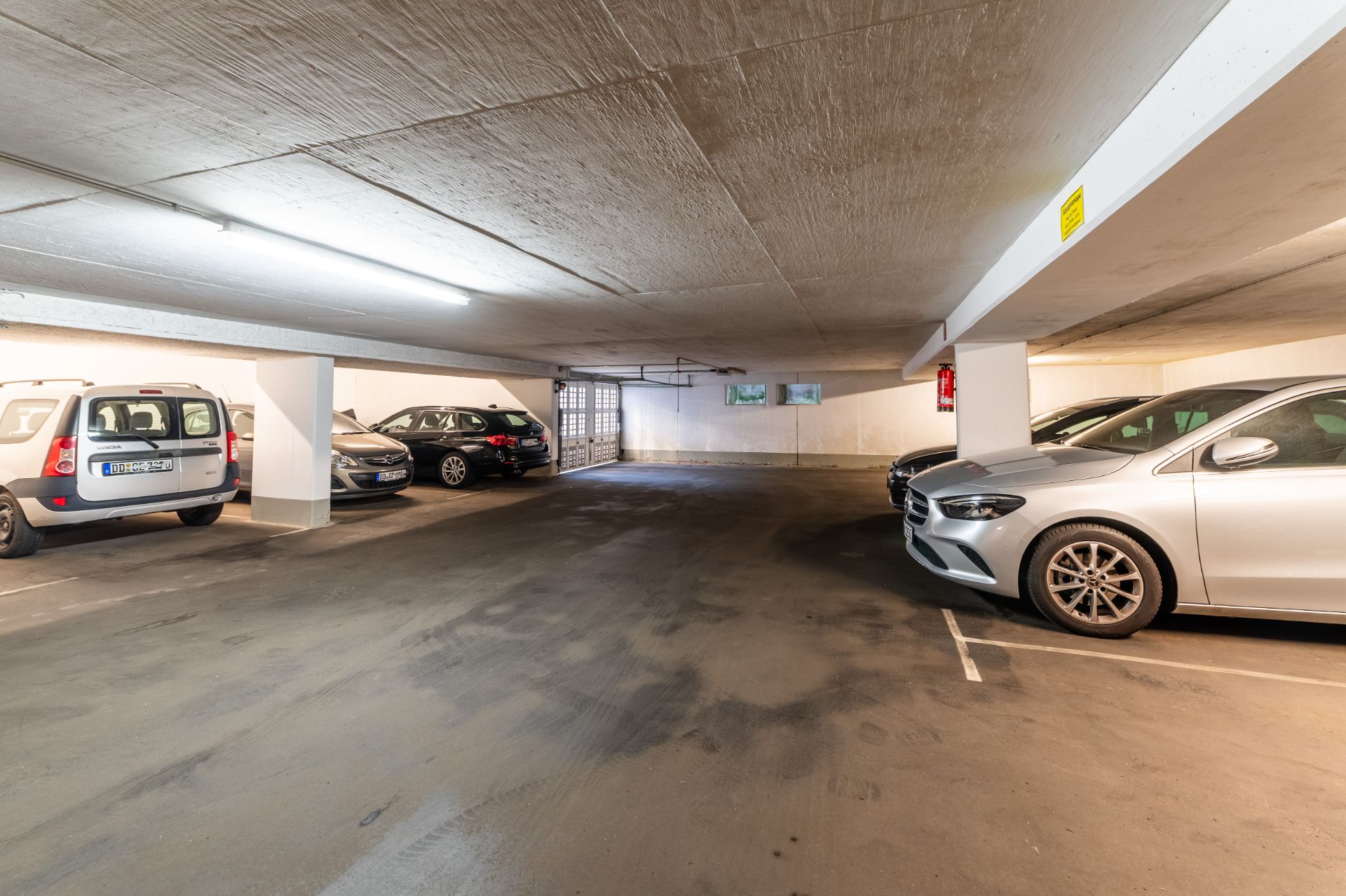 Helle Tiefgarage mit mehreren parkenden Autos und Betonsäulen.