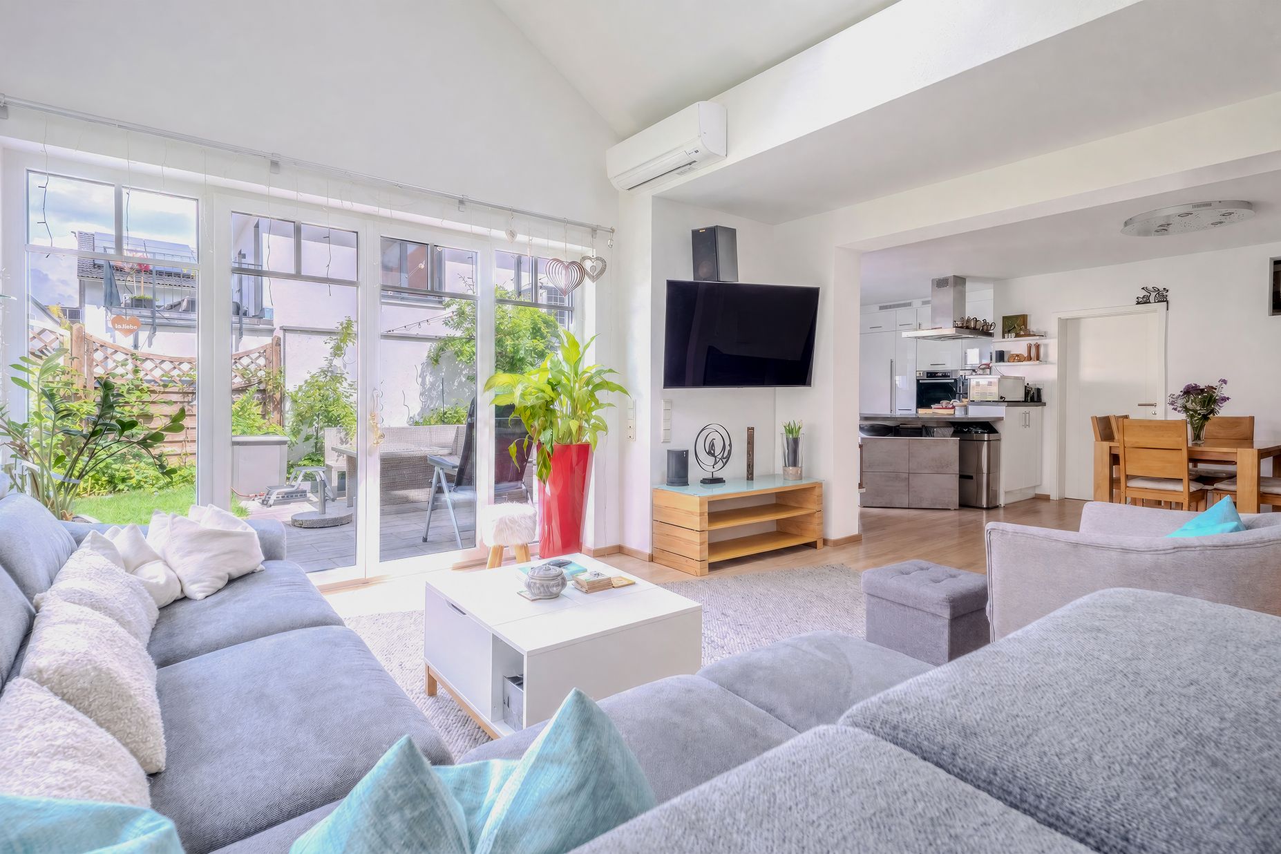 Modernes Wohnzimmer mit grauem Sofa, Couchtisch und Blick auf Terrasse und Garten.