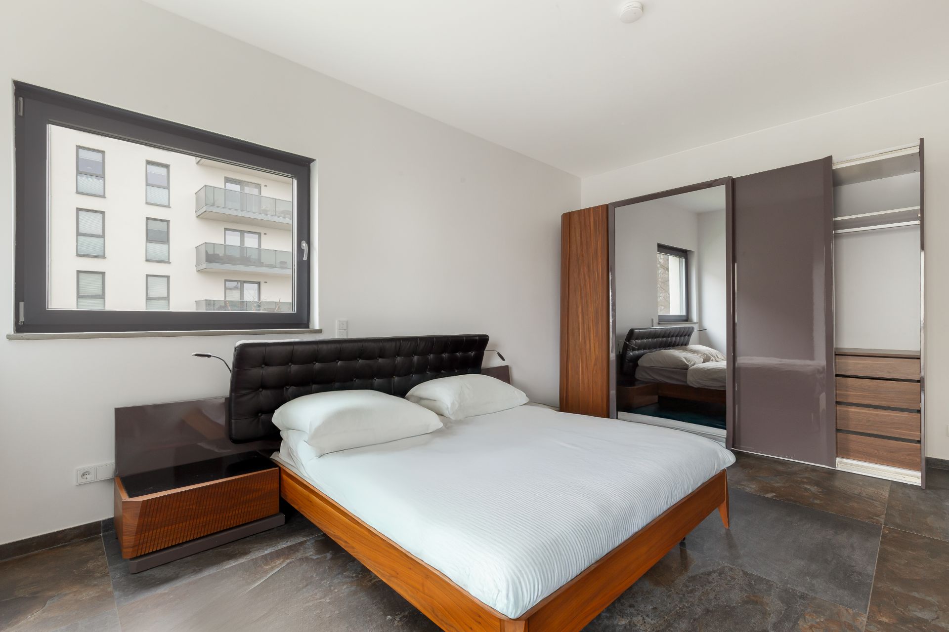 Modernes Schlafzimmer mit Bett, Nachttisch, Fenster und Spiegelschrank.
