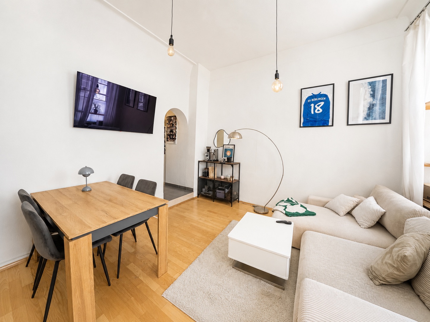 Wohnzimmer mit heller Eckcouch, Holztisch, Fernseher und Wanddekoration.