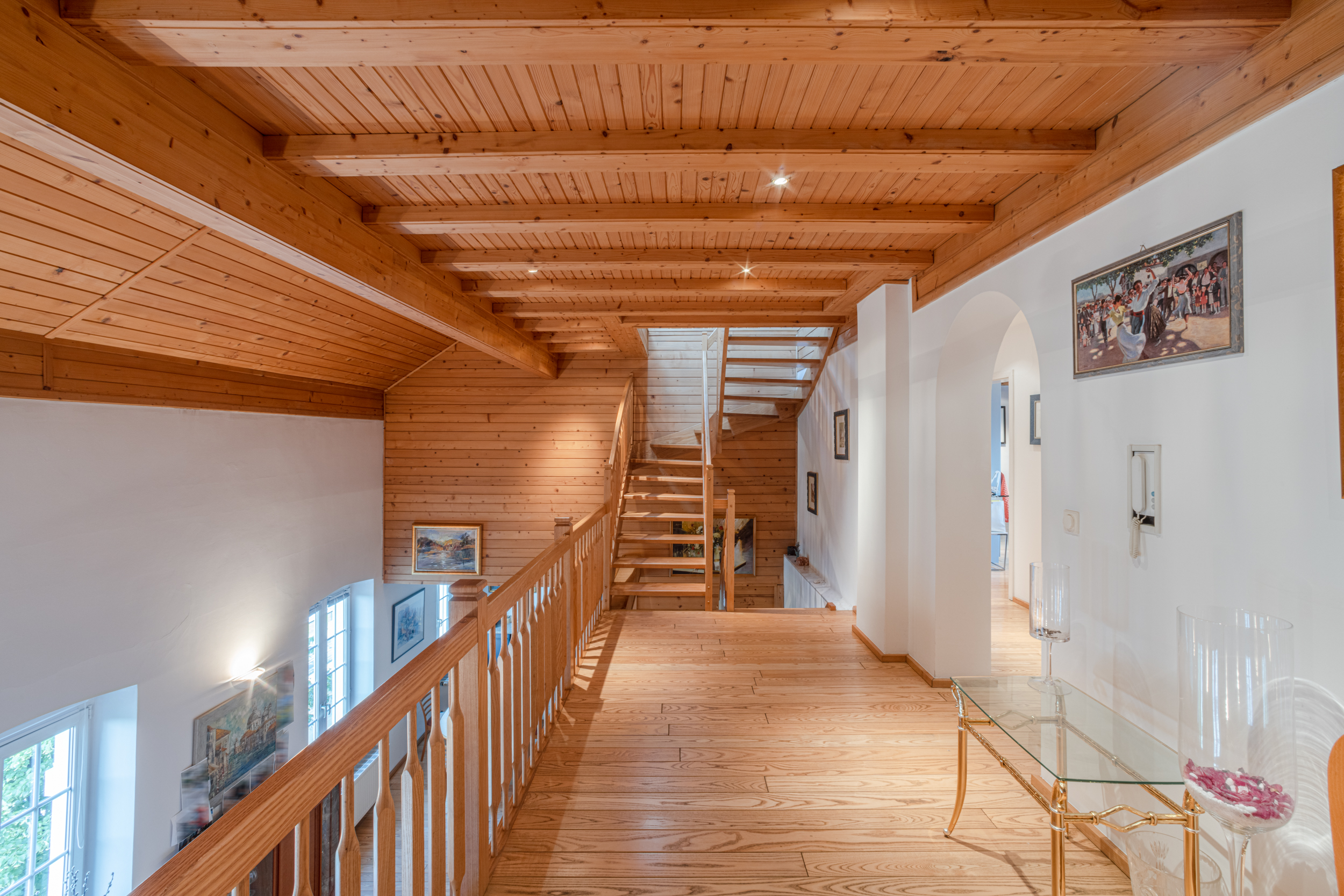 Obergeschossflur mit Holzdecken, Treppe und Glas-Konsole, dekoriert mit Bildern an den Wänden.
