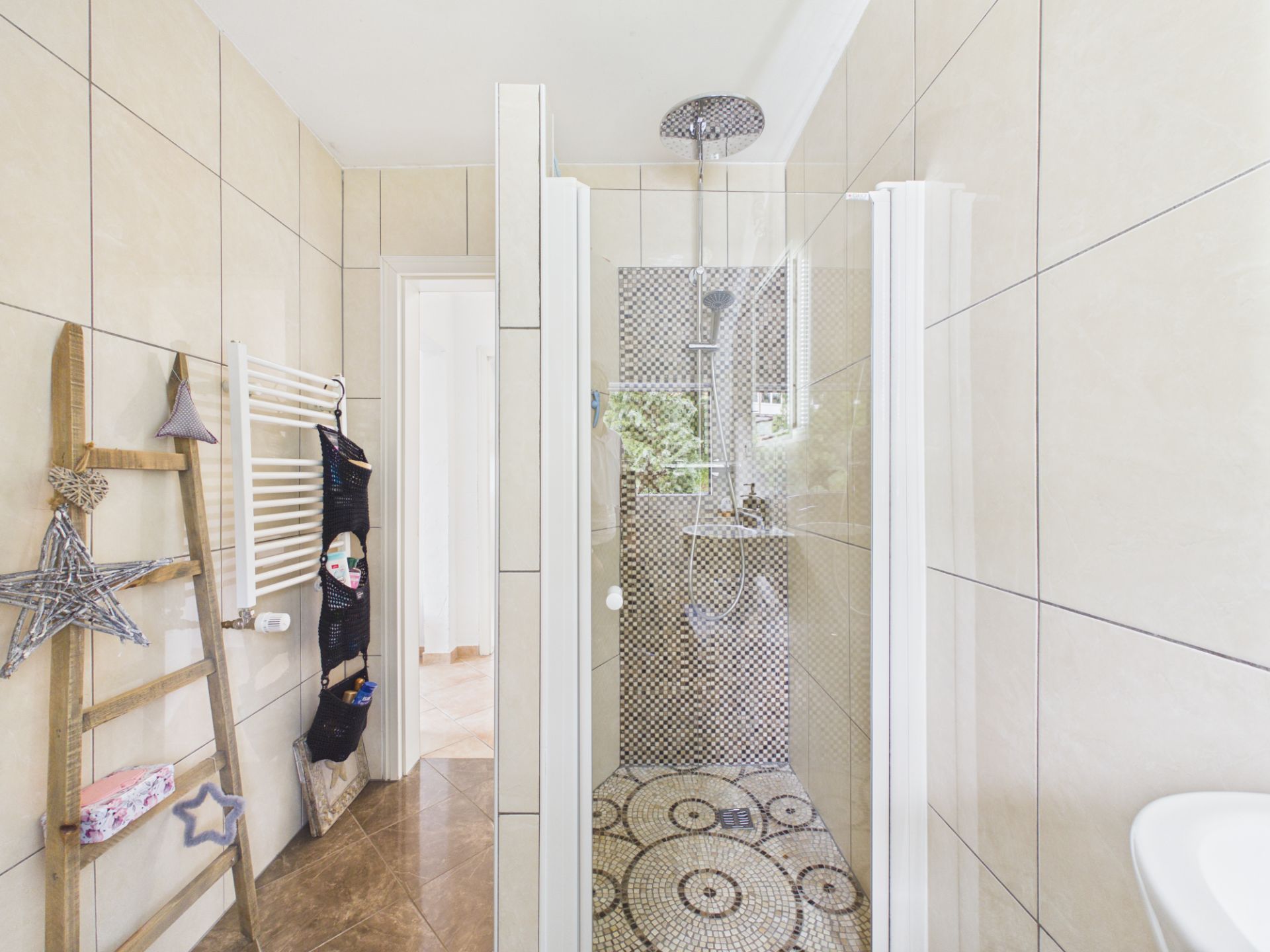 Helles Badezimmer mit begehbarer Dusche, Handtuchheizkörper und dekorativer Holzleiter.