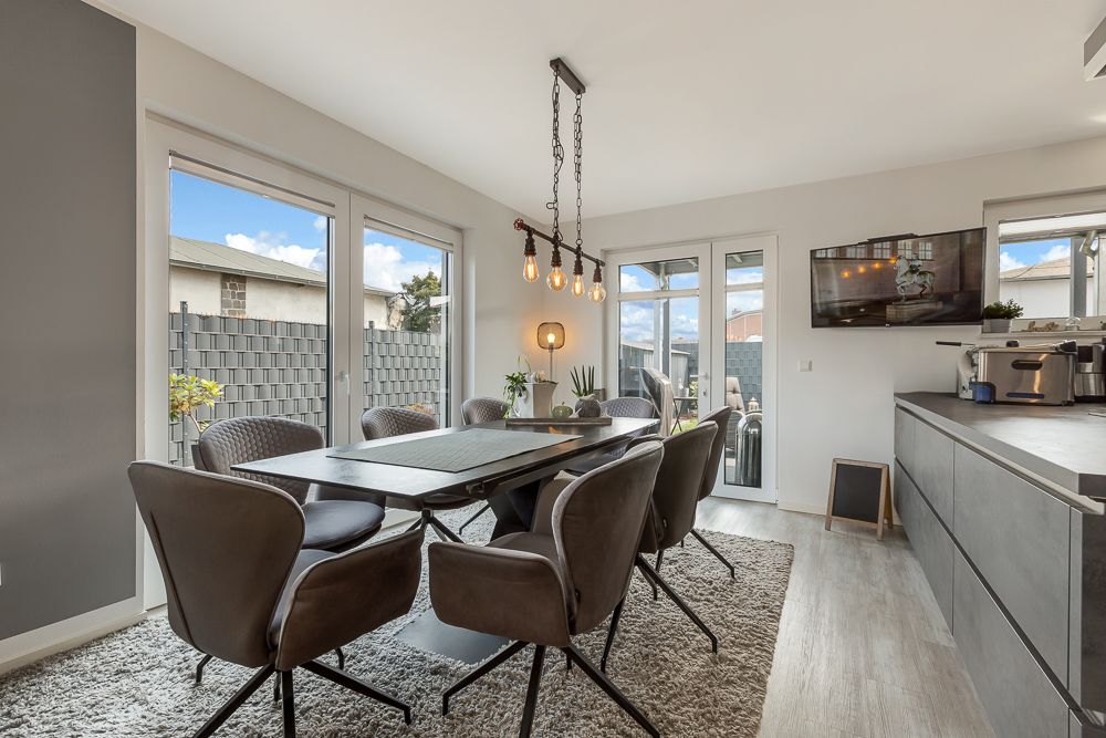 Esszimmer mit großem Tisch, sechs Stühlen, Teppich, Hängelampe und Zugang zur Terrasse.