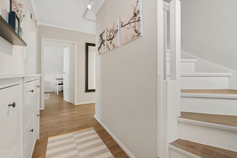 Heller Flur mit Holztreppe, Holzfußboden, weißen Wänden und dekorativen Bildern.