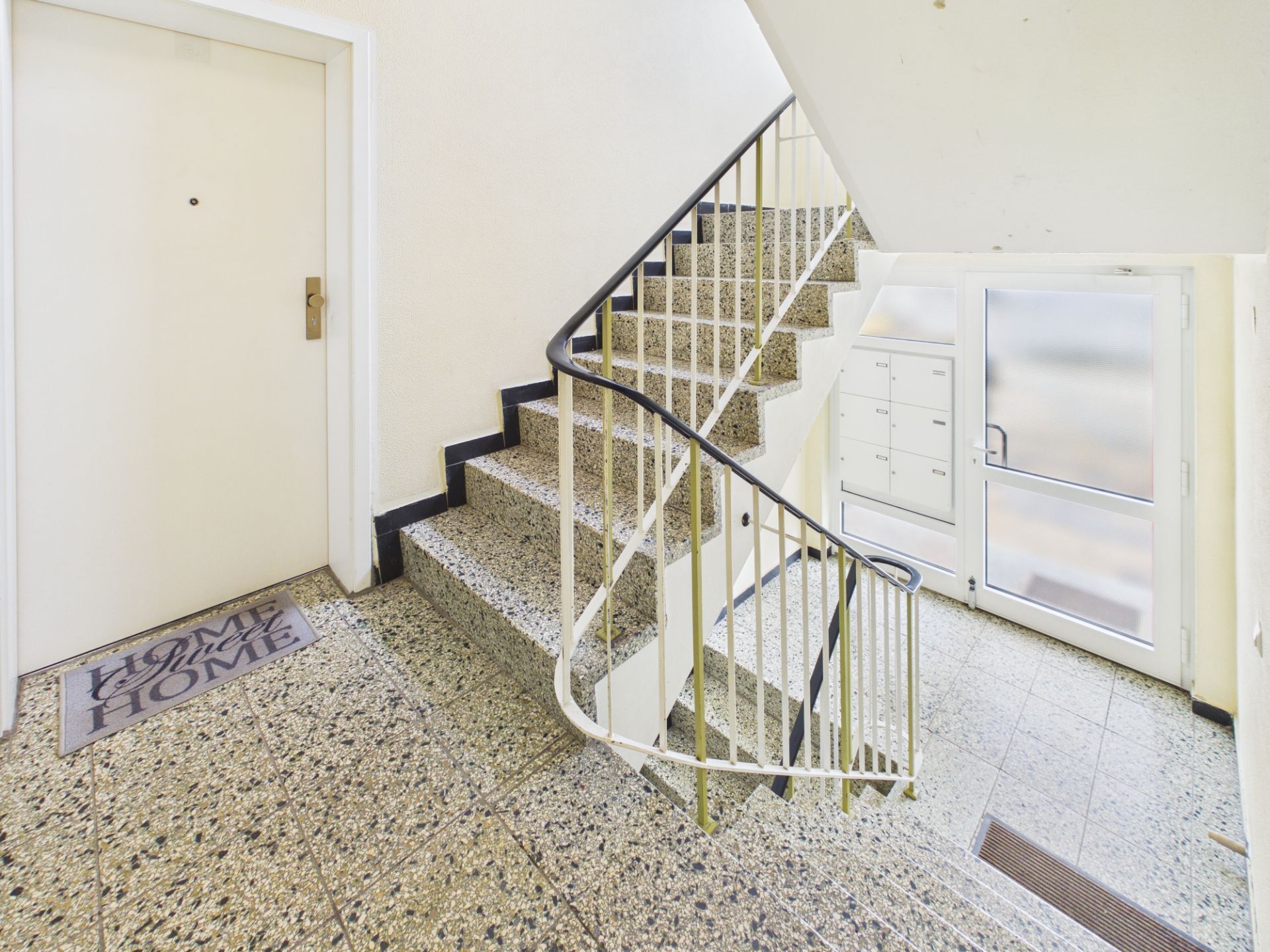 Heller Treppenhausbereich mit Briefkästen, Eingangstür und Fußmatte vor Wohnungstür.
