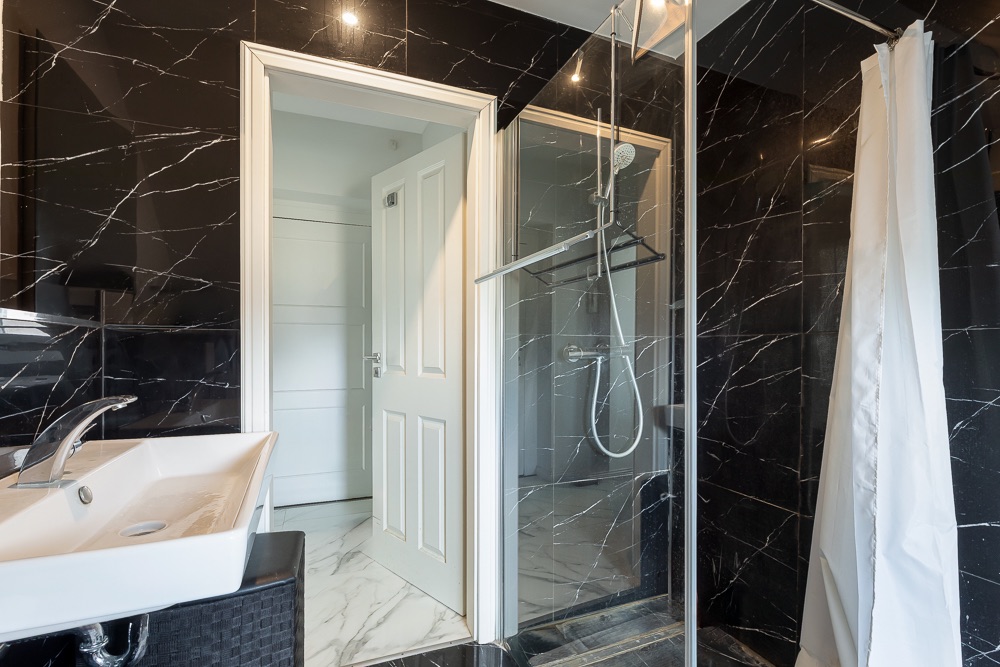 Modernes Bad mit schwarzer Marmorverkleidung, Waschbecken und verglaster Dusche.