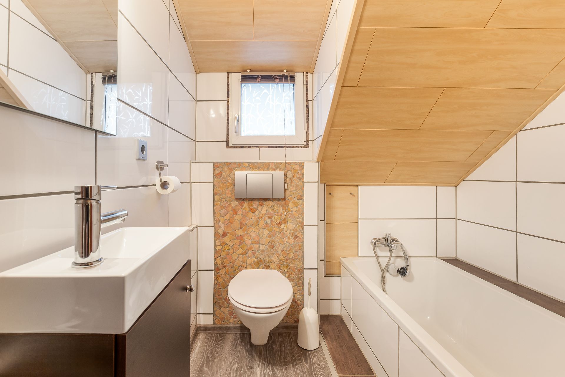 Modernes Badezimmer mit Waschbecken, Toilette, Badewanne und kleinem Fenster unter Dachschräge.