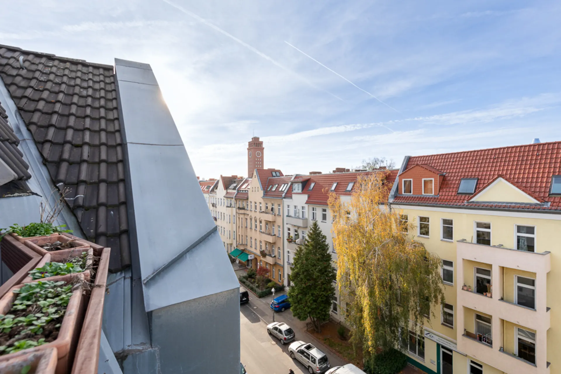 Blick von einem Balkon auf Wohnhäuser mit roten Dächern und eine ruhige Straße.