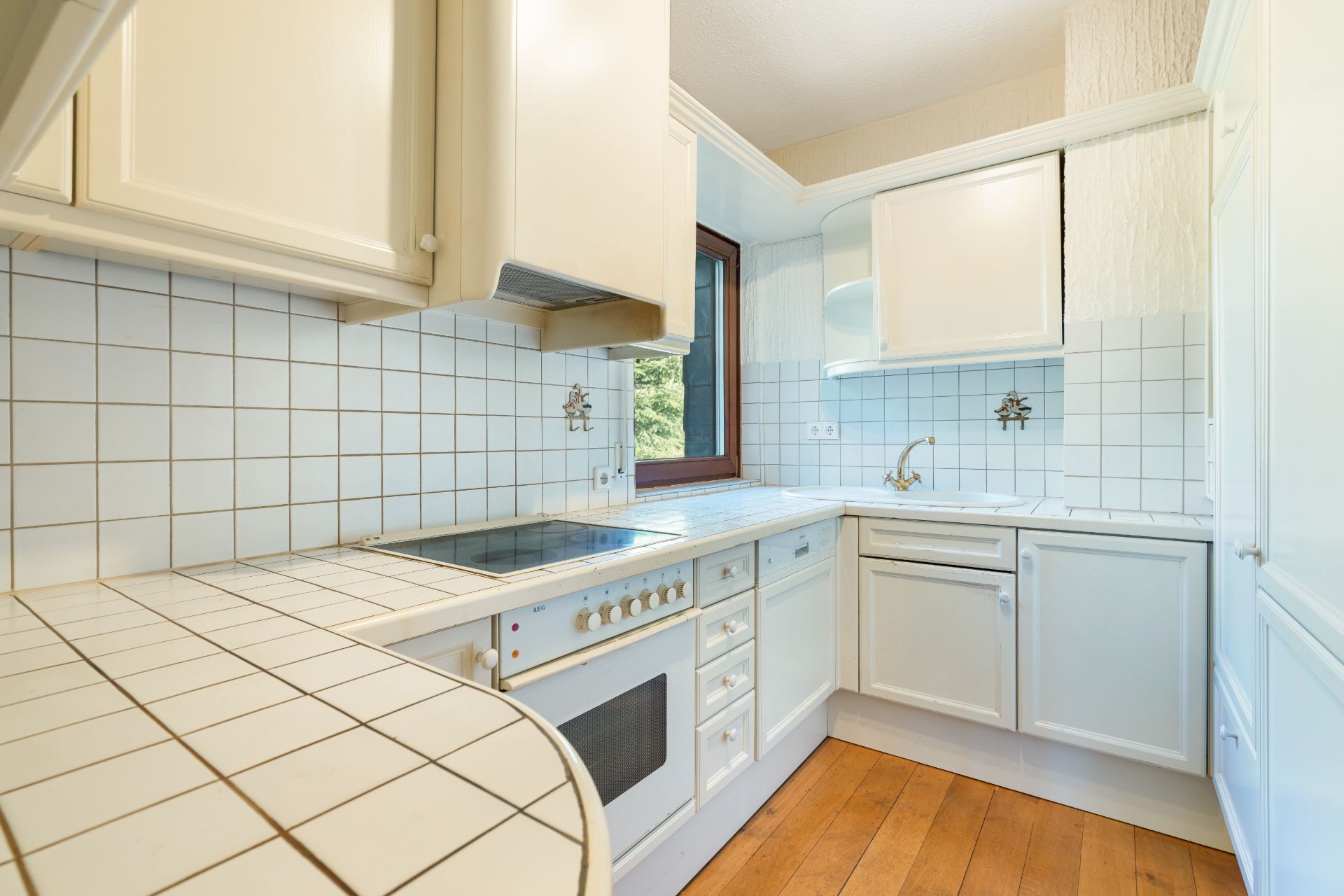 Helle Einbauküche mit weißen Fliesen, Kochfeld, Backofen und Holzboden.
