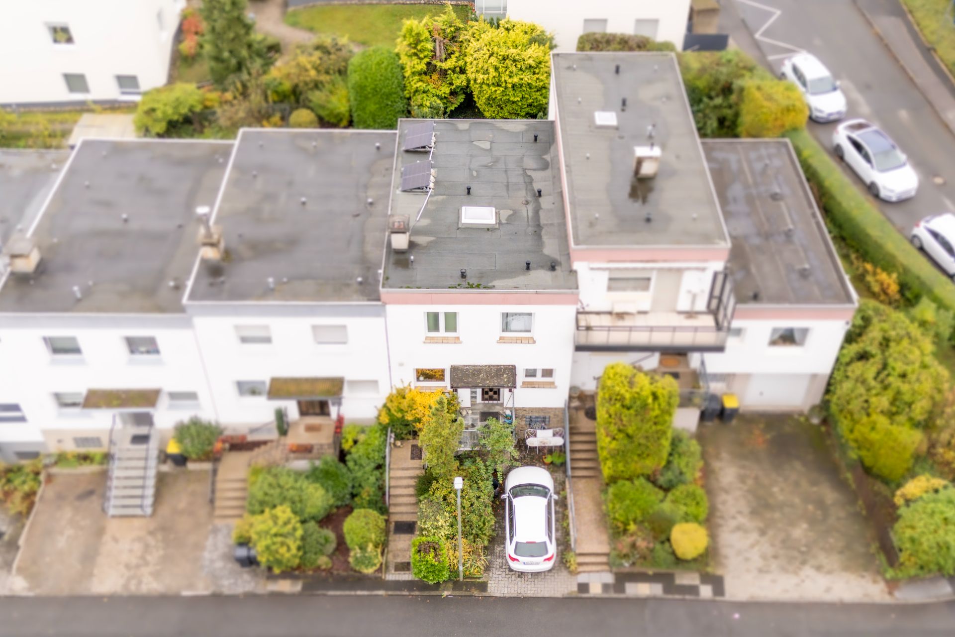 Luftaufnahme eines Wohnhauses mit Garten und einem weißen Auto in der Einfahrt.