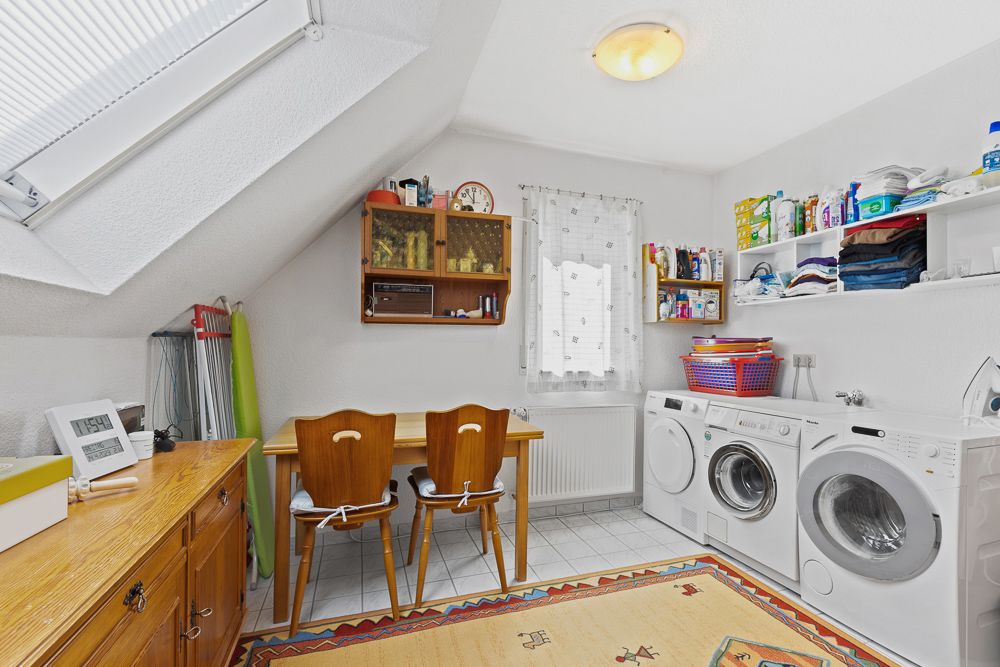Heller Hauswirtschaftsraum mit Waschmaschine, Trockner, Regalen und Tisch mit zwei Stühlen.