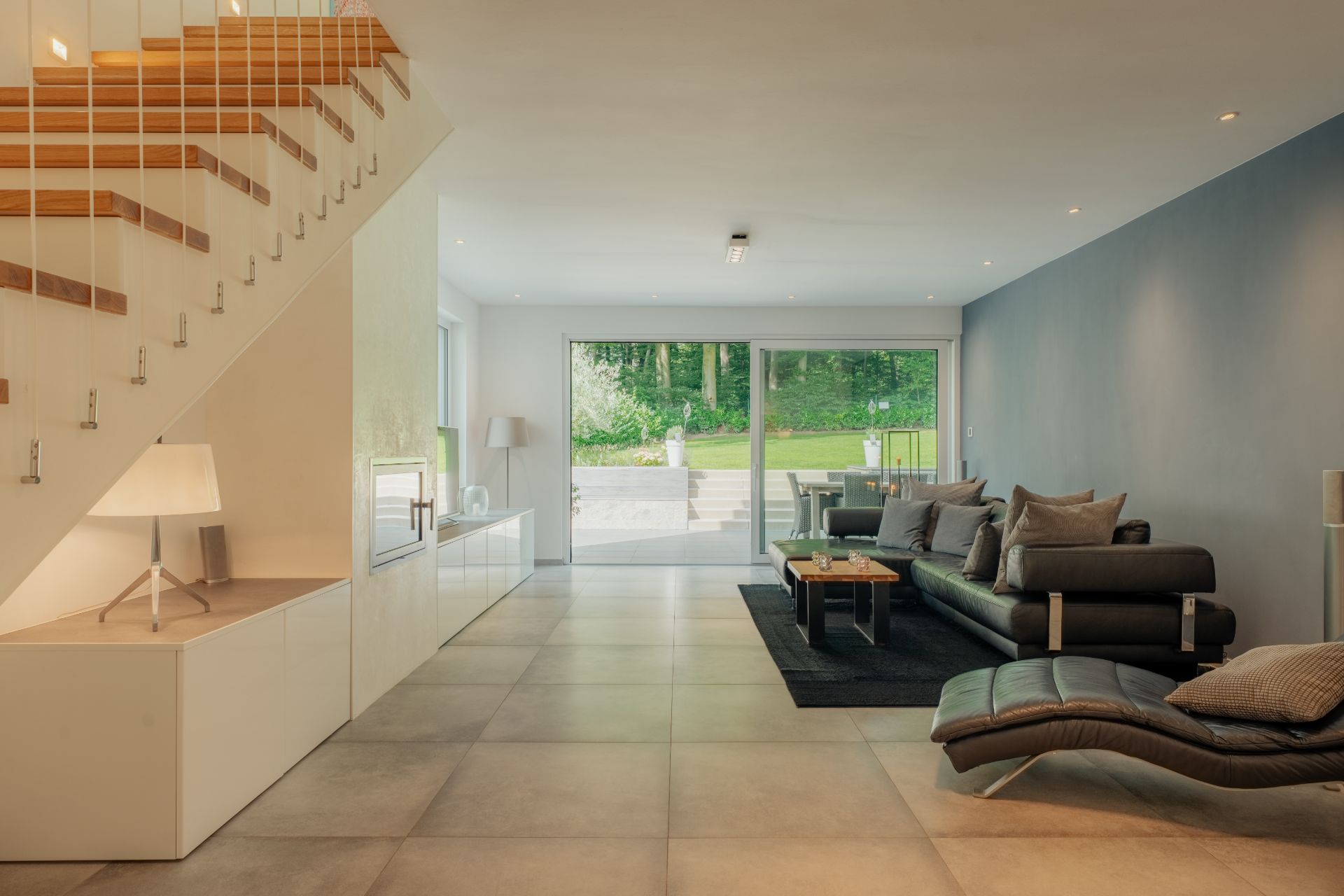 Modernes Wohnzimmer mit großen Sofas, Glas-Schiebetür zum Garten und Treppe mit Holzstufen.