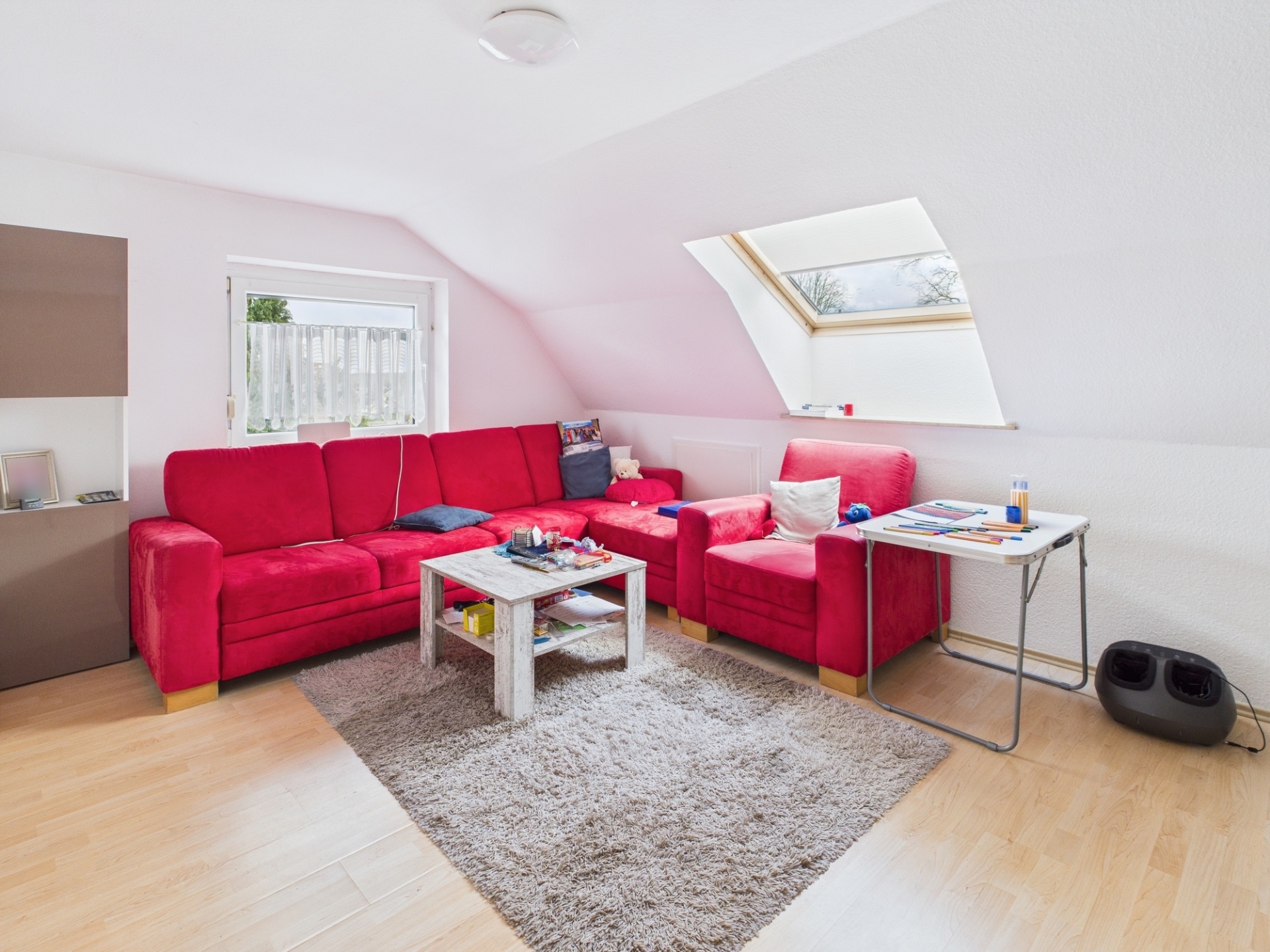 Wohnzimmer mit rotem Sofa, Teppich, Couchtisch und Dachfenster.