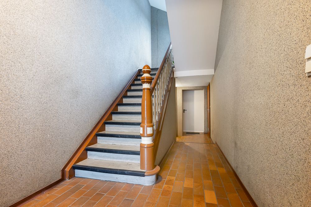 Flur mit Treppe und braunem Fliesenboden in einem Wohngebäude.