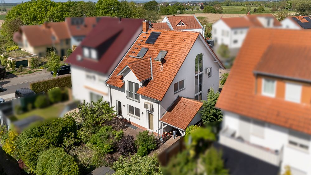 Zweistöckiges Haus mit rotem Ziegeldach, Garten und angrenzenden Häusern in Wohngegend.