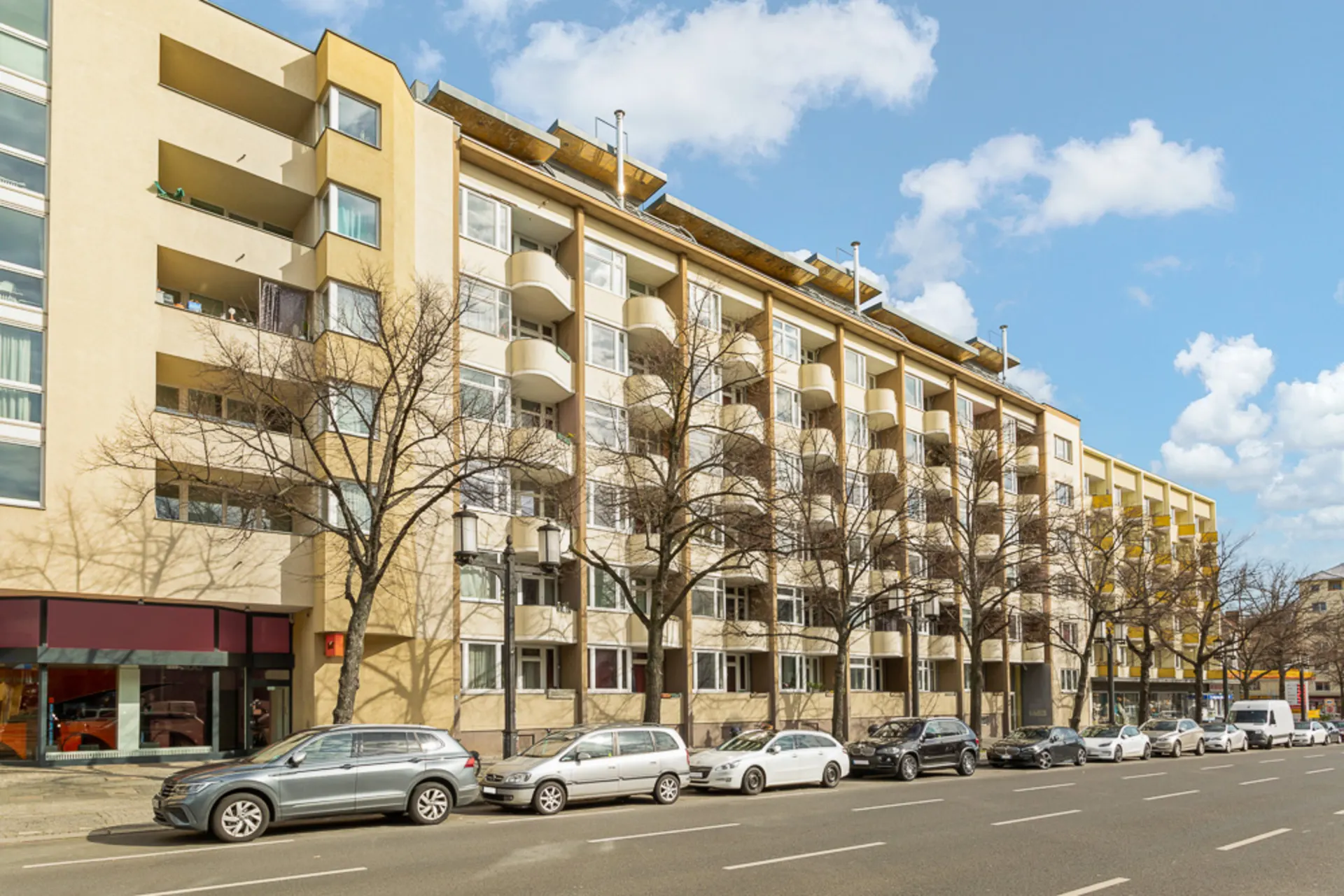 Mehrstöckiges Wohngebäude mit Balkonen und geparkten Autos an einer Straße.