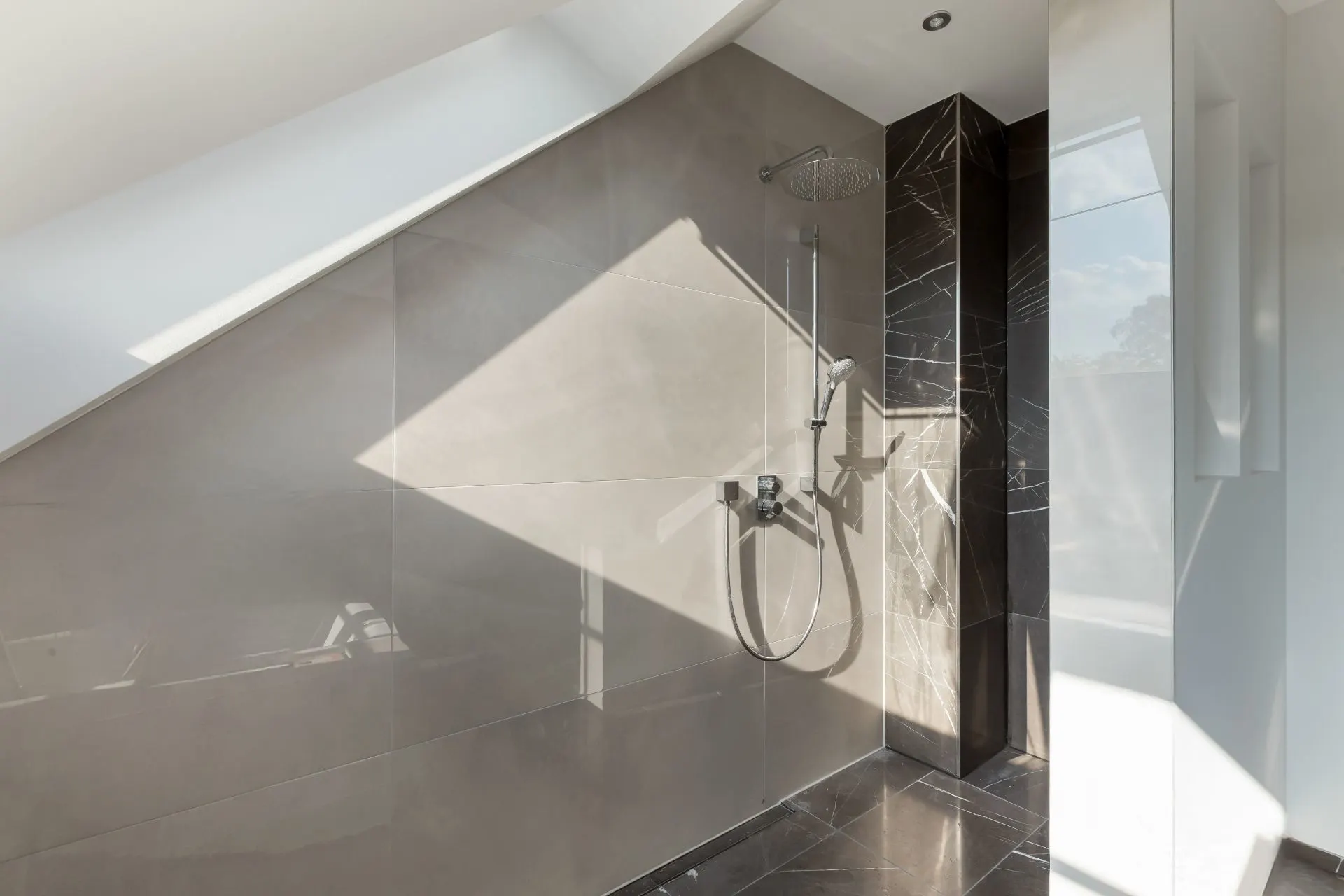 Moderne, offene Dusche mit Regenduschkopf und großen Fliesen an Wand und Boden.