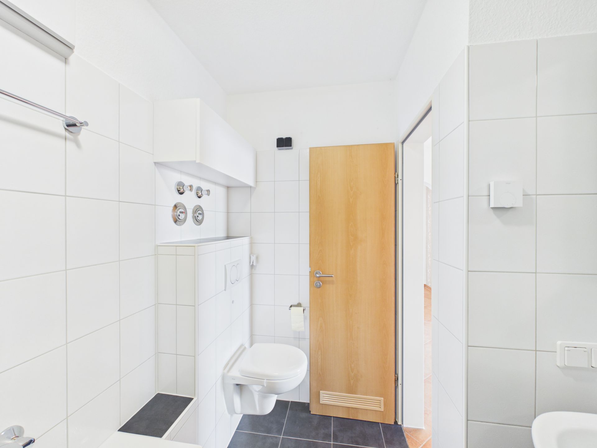 Helles, gefliestes Badezimmer mit Wandtoilette und Holztür.