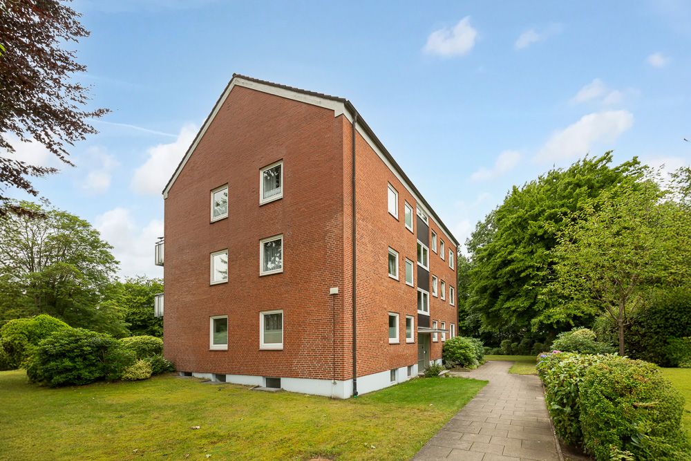 Rotes Mehrfamilienhaus mit vielen Fenstern und umgebendem Garten.