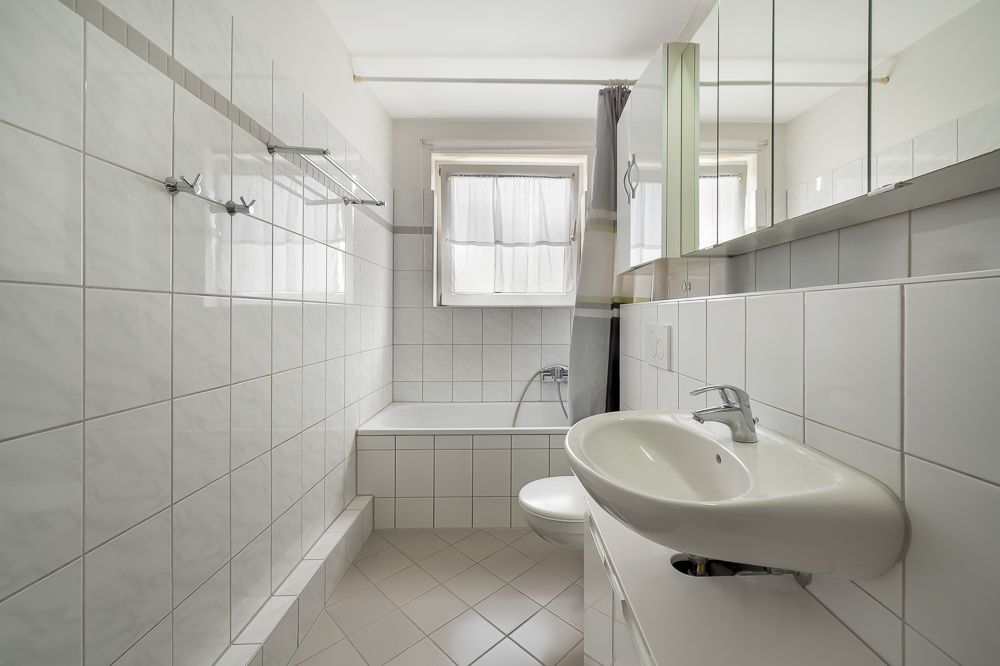 Helles, gefliestes Badezimmer mit Badewanne, Waschbecken und Fenster.