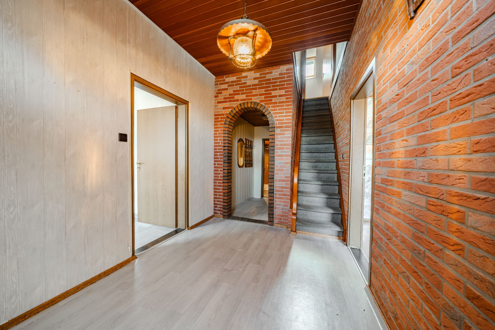 Flur mit Holzboden, Ziegelwänden, Treppe und einem Rundbogen.
