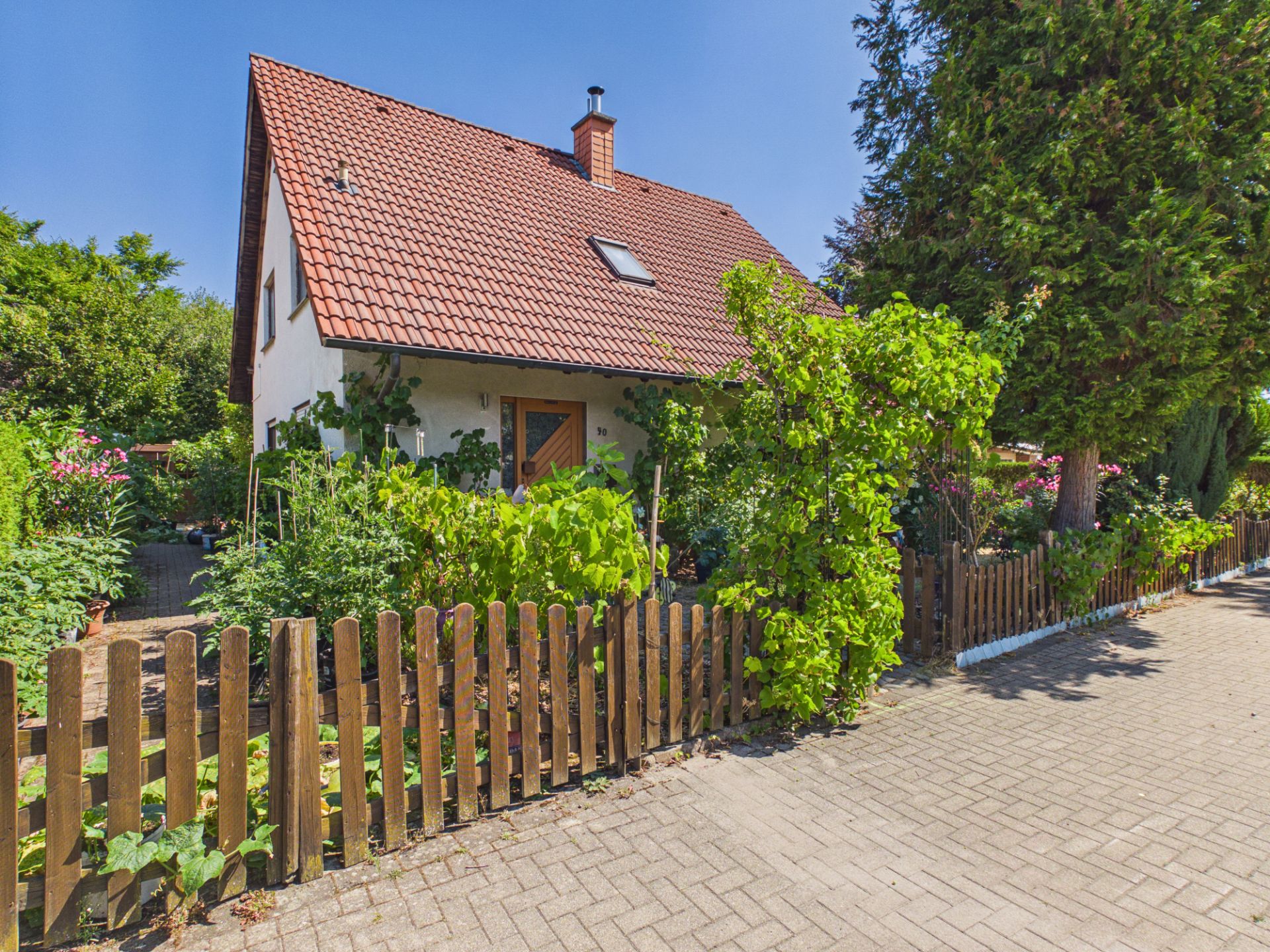 Haus mit rotem Dach und Holzzaun, umgeben von grünem Garten und Bäumen.
