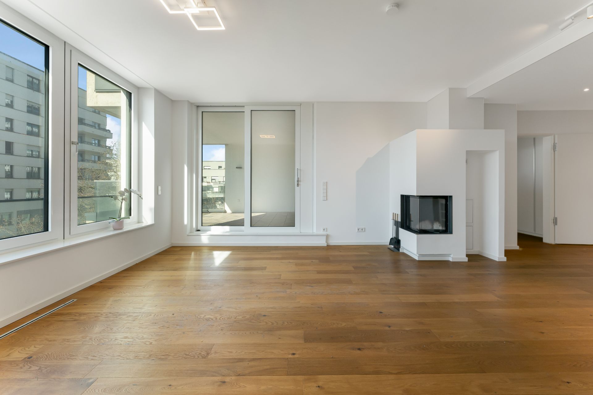 Helles Wohnzimmer mit großen Fenstern, Holzboden, Kamin und Zugang zu einem Balkon.