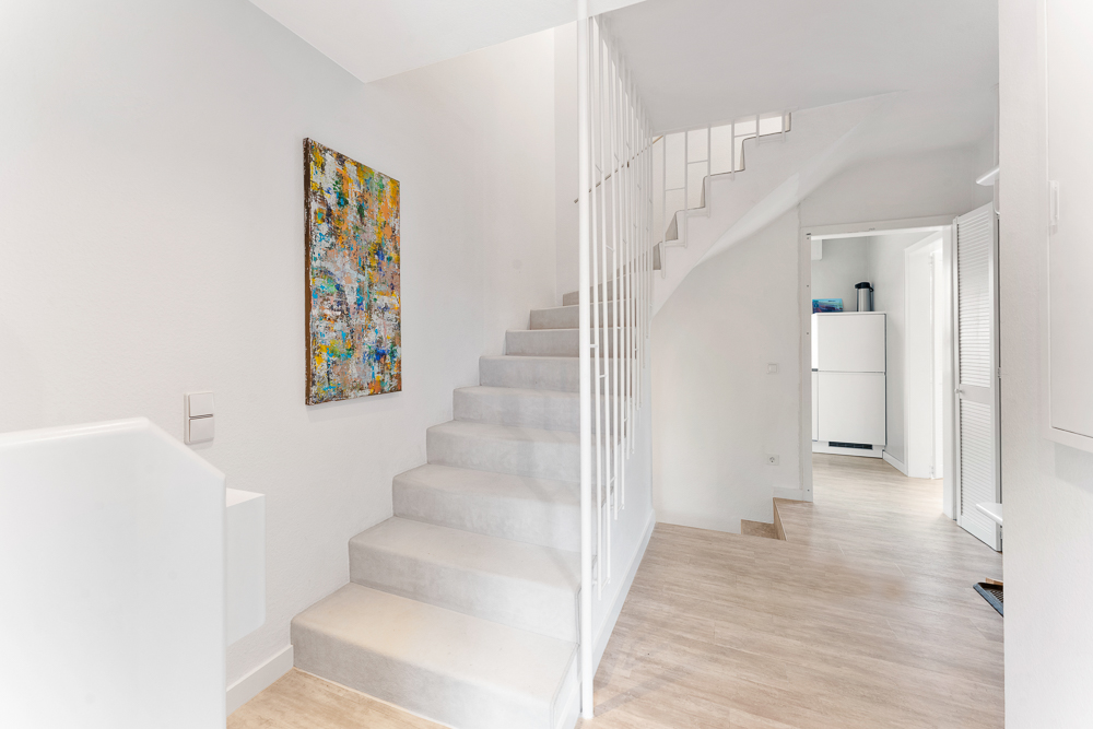 Heller Flur mit Treppe, farbigem Bild an der Wand und Holzboden.
