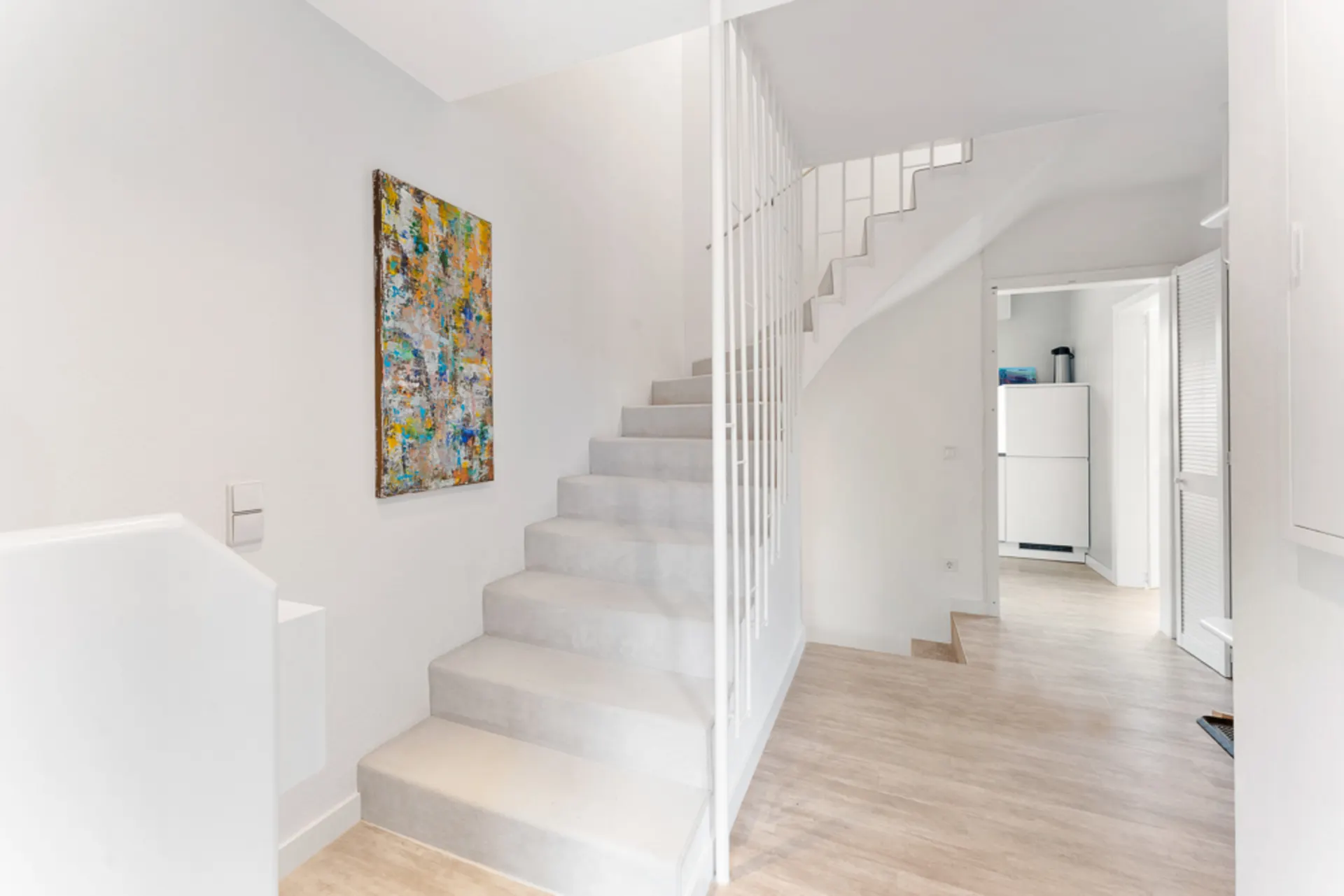 Heller Flur mit Treppe, farbigem Bild an der Wand und Holzboden.