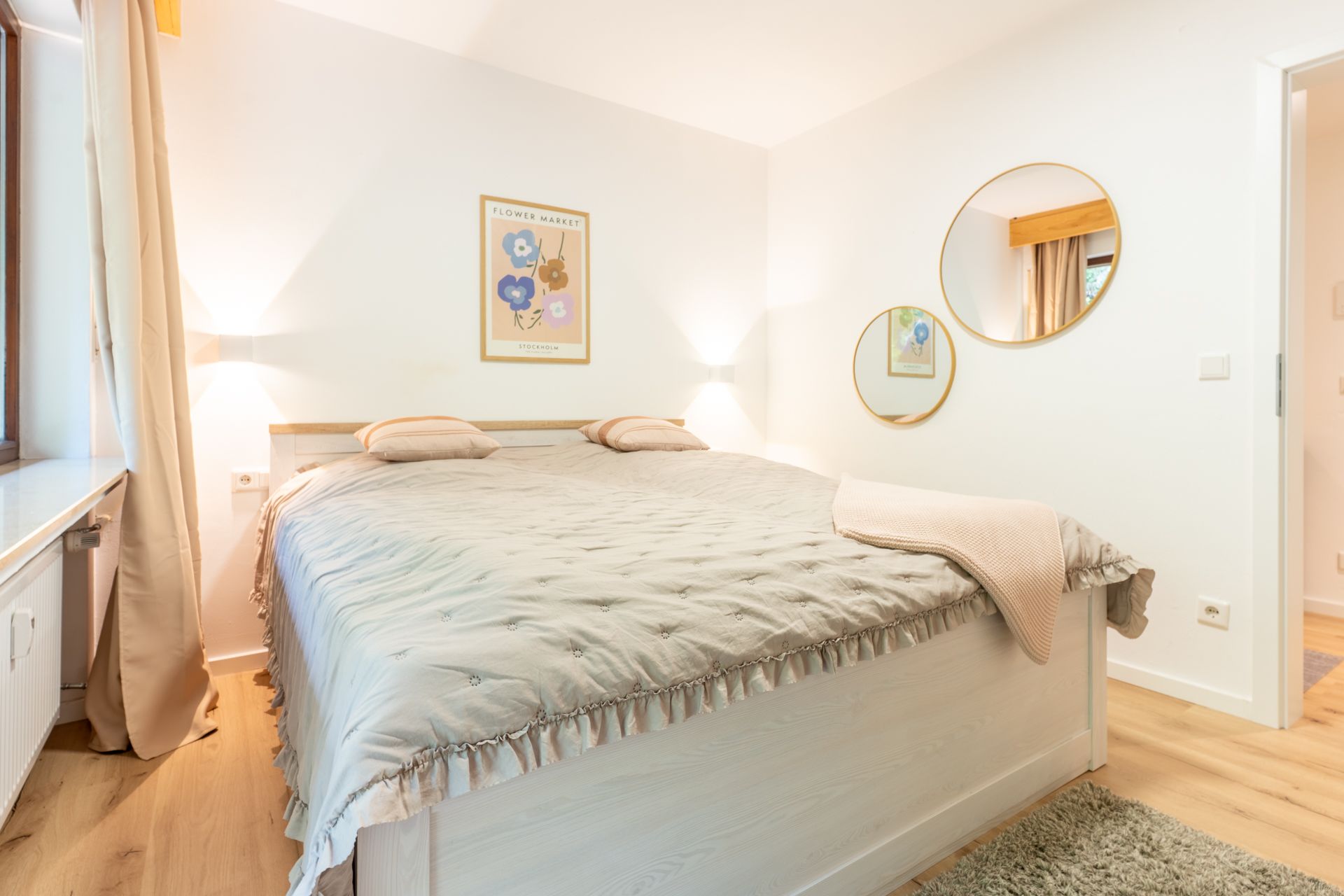 Helles Schlafzimmer mit großem Bett, zwei runden Spiegeln und einem Poster an der Wand.