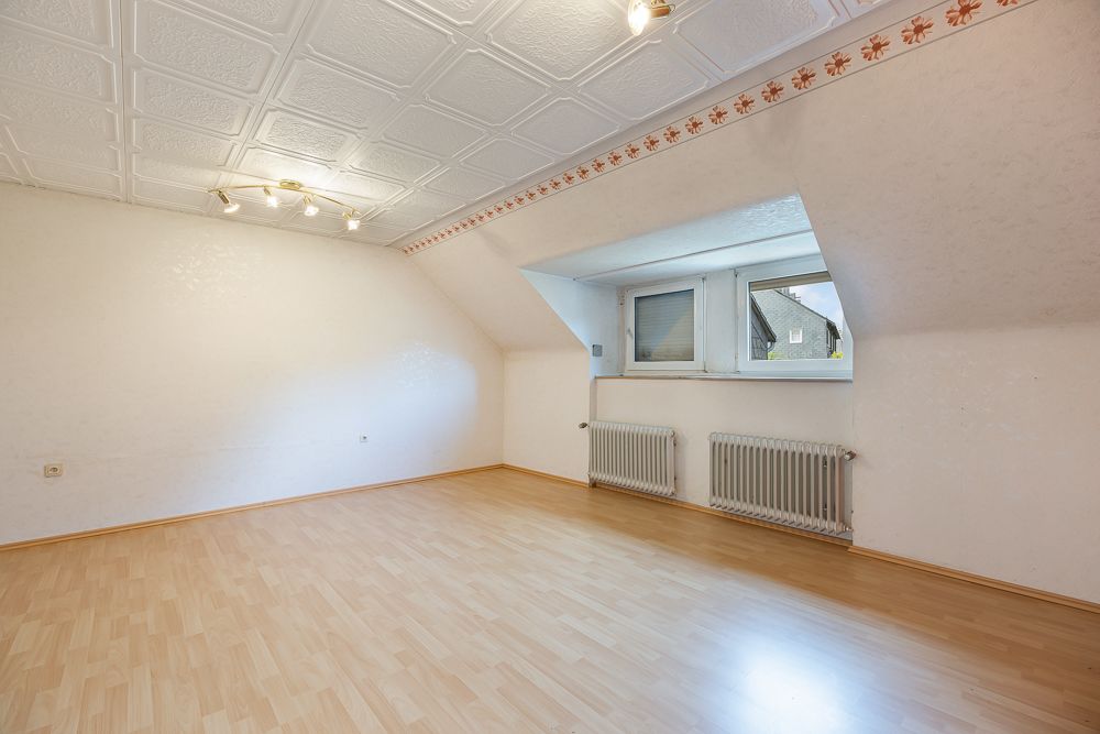 Helles Zimmer mit Laminatboden, Fenster in Gaube und zwei Heizkörpern unter dem Fenster.