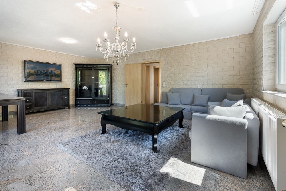 Helles Wohnzimmer mit grauem Sofa, schwarzem Tisch, Kronleuchter und großem Fenster.