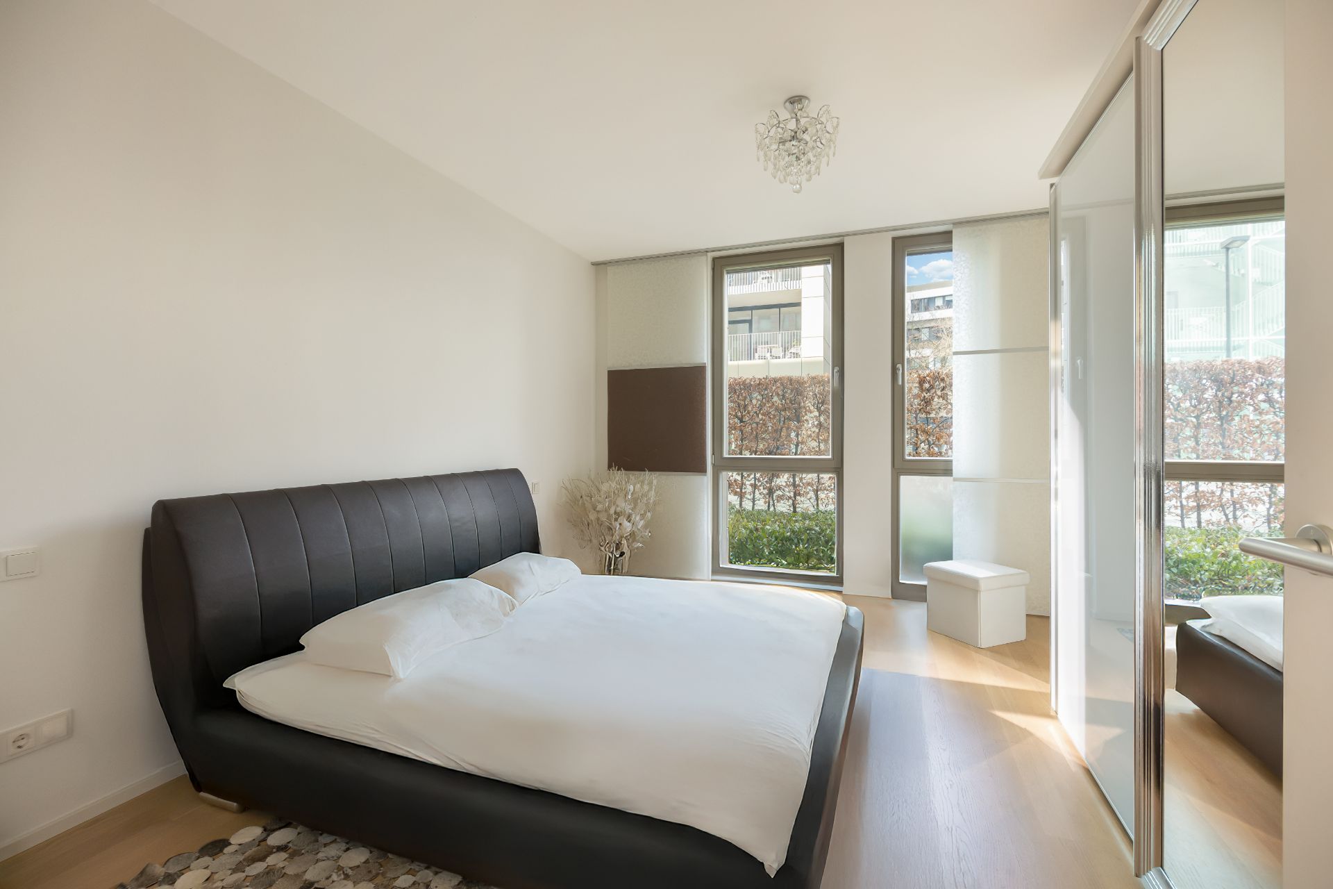 Helles Schlafzimmer mit großem Bett, bodentiefen Fenstern und Spiegel-Schiebetür.