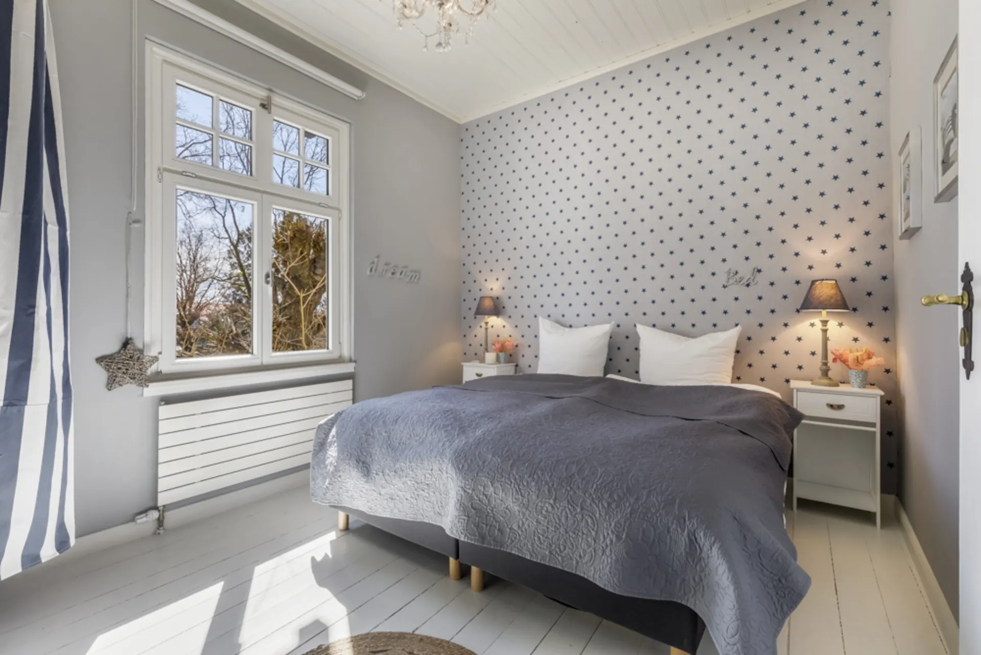 Helles Schlafzimmer mit Doppelbett, Nachttischen, sternengemusterter Wand und großem Fenster.