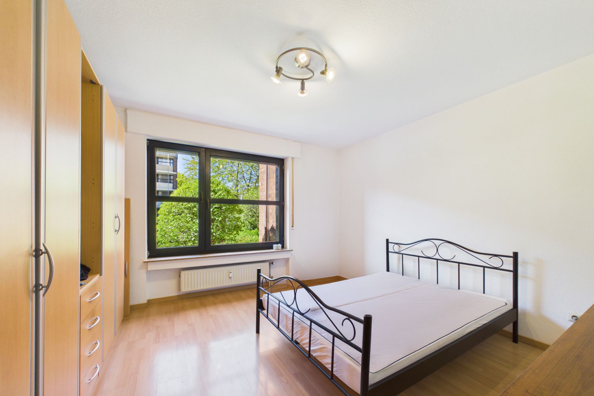 Helles Schlafzimmer mit Doppelbett, großem Fenster und Einbauschrank auf Holzfußboden.