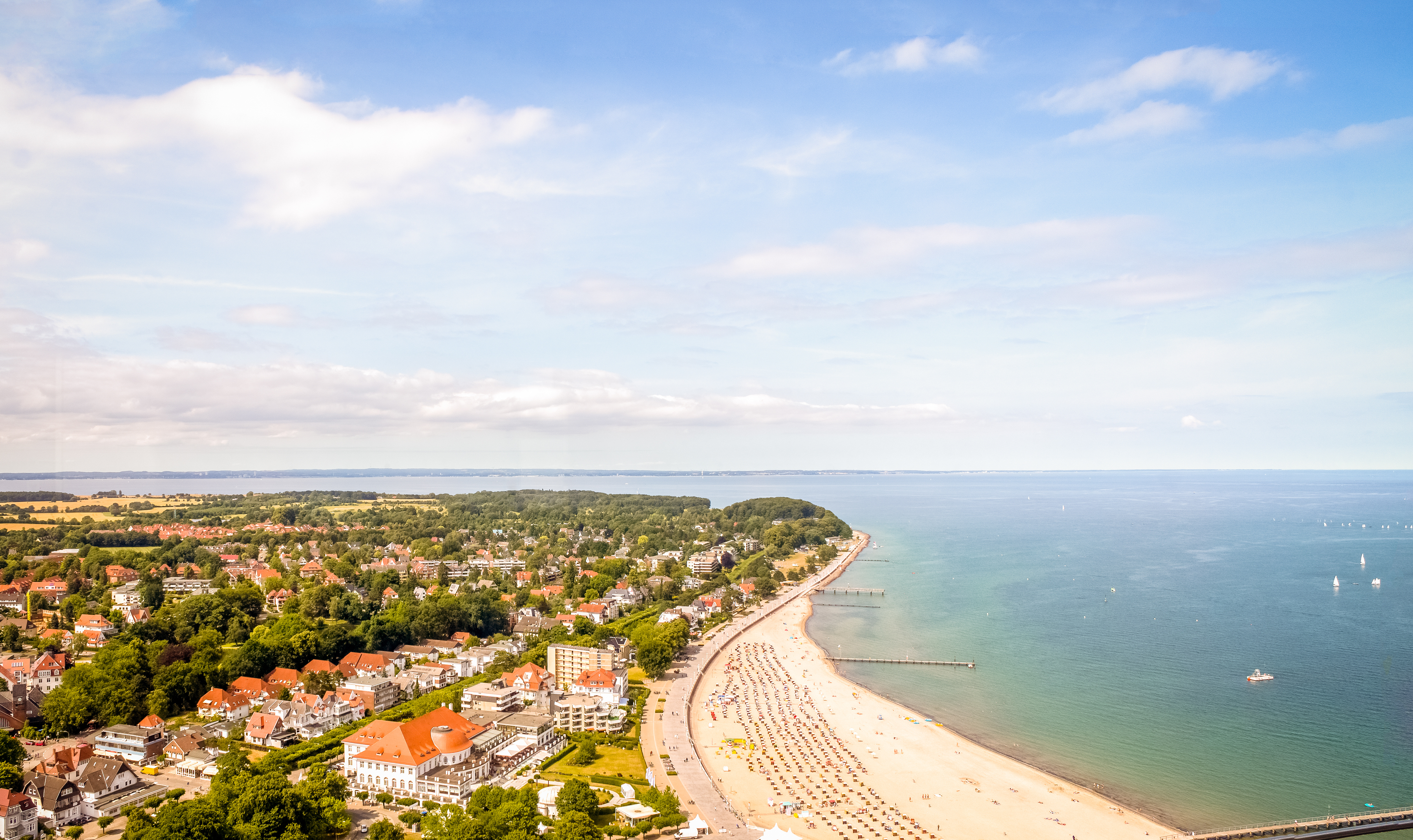 Luftaufnahme einer Küstenstadt mit Sandstrand, Häusern und grünem Hinterland.