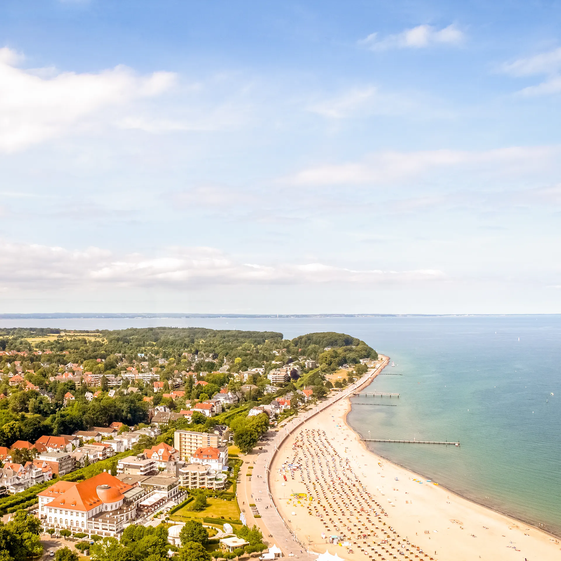 Luftaufnahme einer Küstenstadt mit Sandstrand, Häusern und grünem Hinterland.