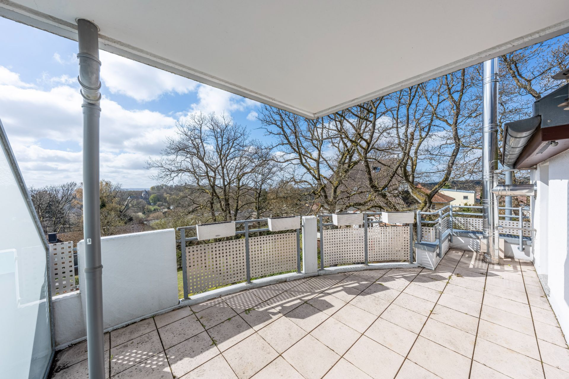 Überdachter Balkon mit Fliesenboden und Blick auf Bäume und Häuser.